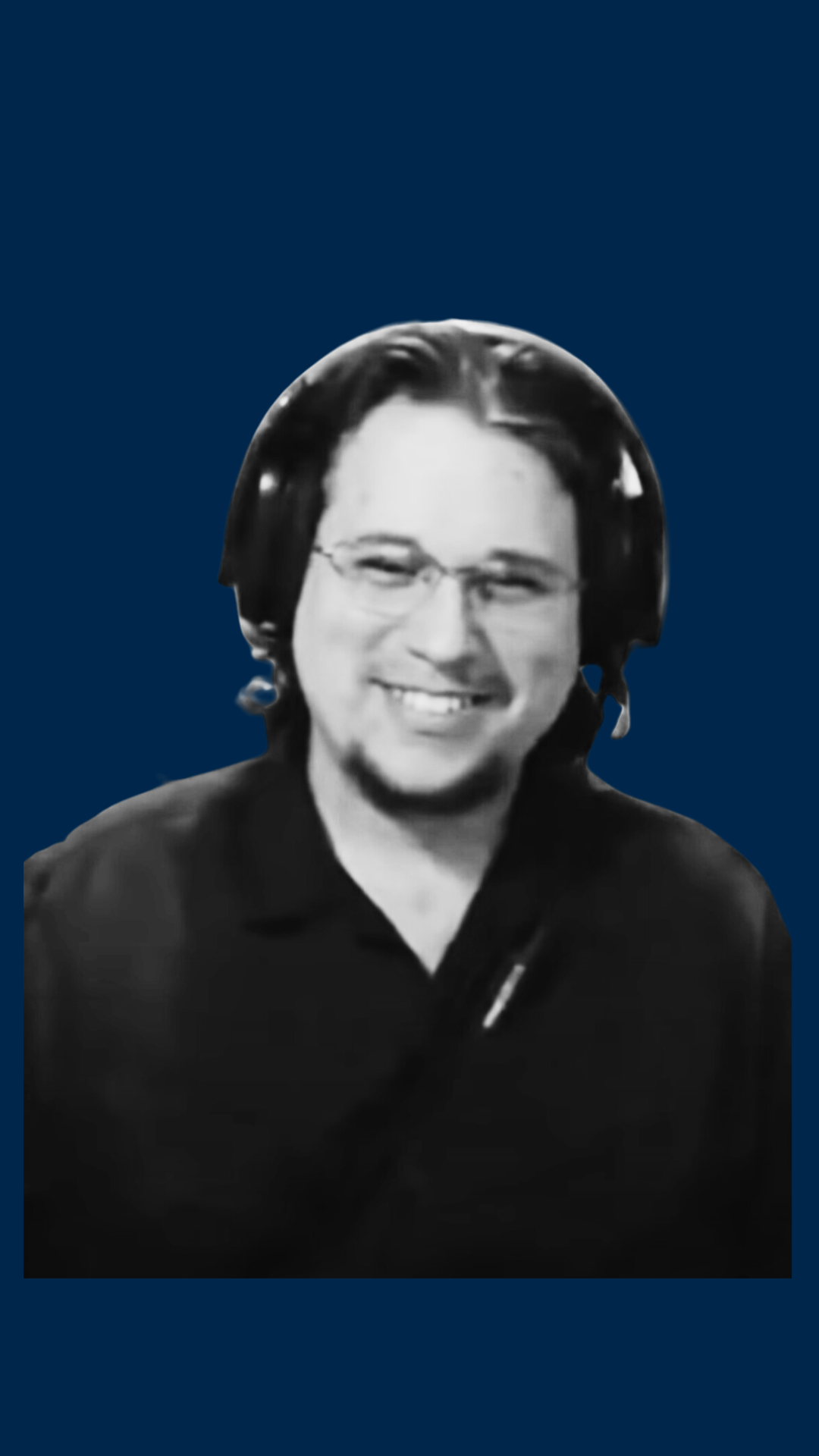 Black and white photo of a smiling man wearing glasses and headphones, dressed in a black shirt, against a solid blue background.