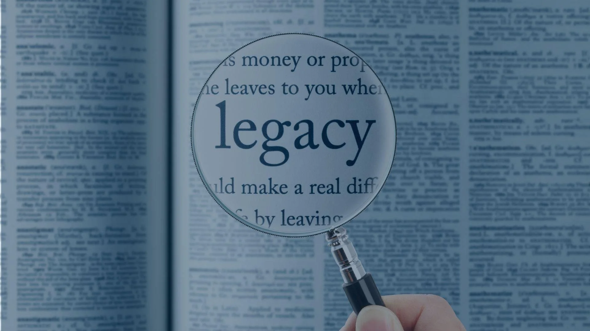 Hand holding a magnifying glass over a newspaper page with the word 'legacy' in focus.