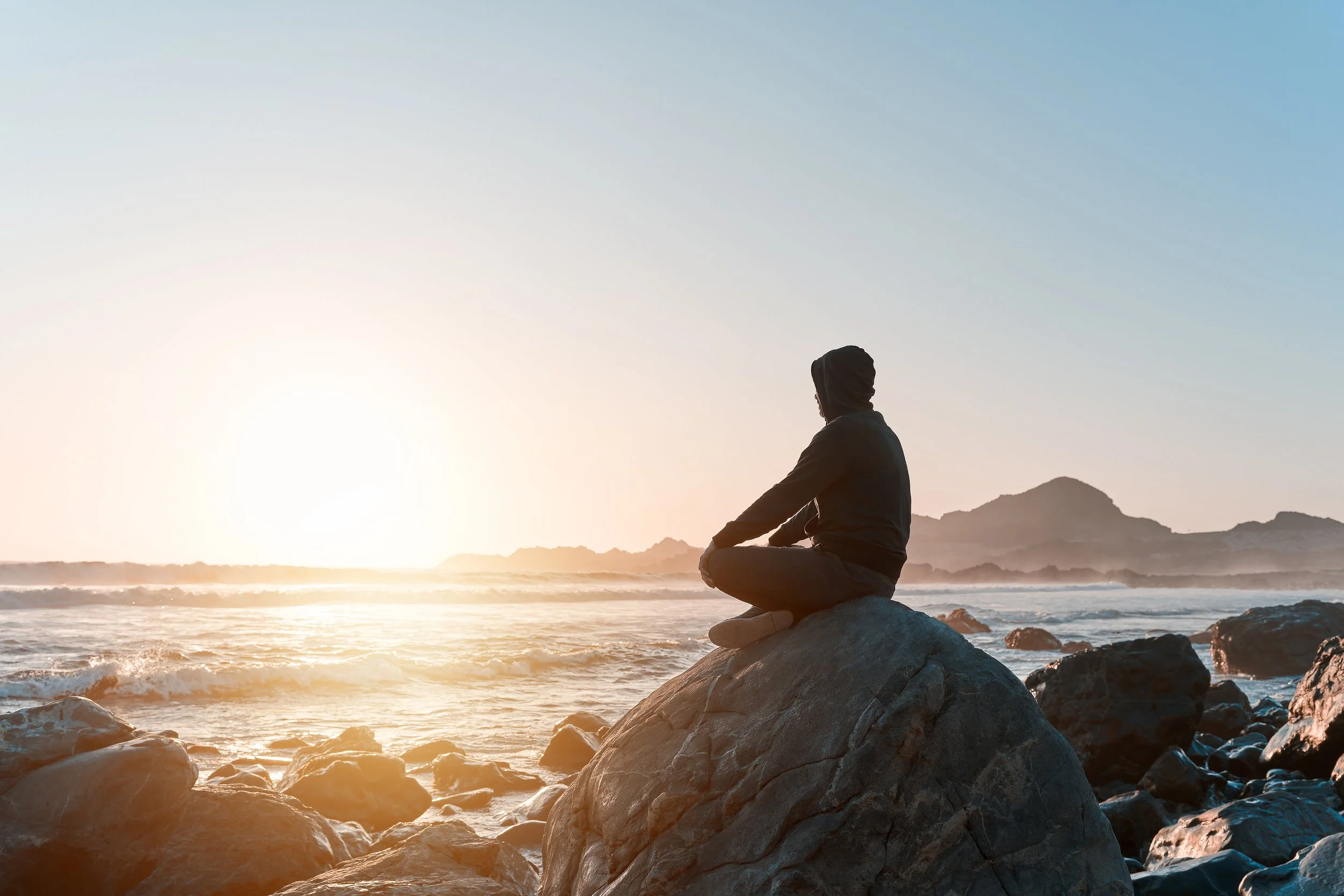Man sitting on a rock by the ocean. He is calm and peaceful and is using Inner-relationship Focusing, an embodied mindfulness practice for healing and self-connection.