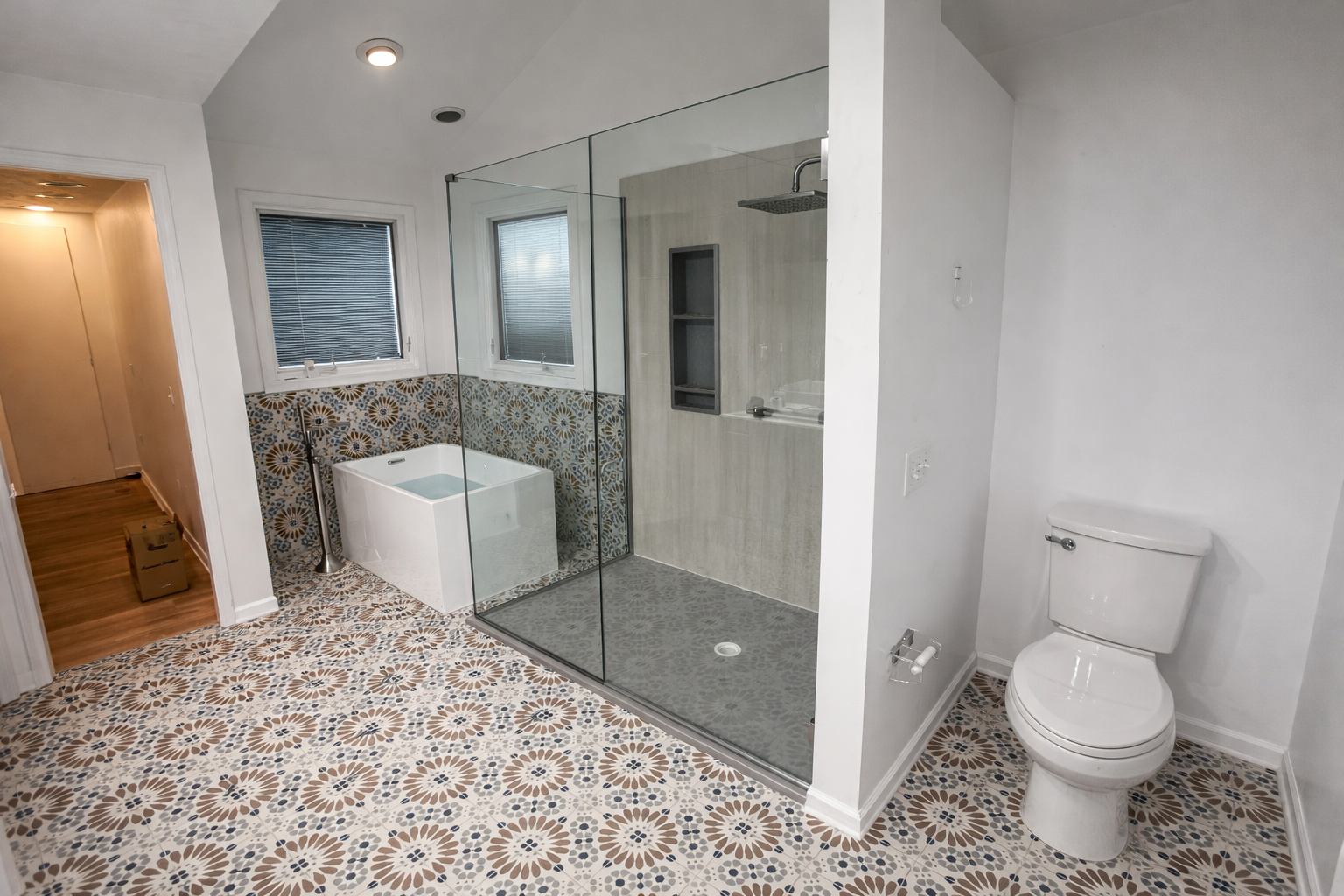 Bathroom with patterned tile floor, glass-enclosed shower, white toilet, and windows with blinds.