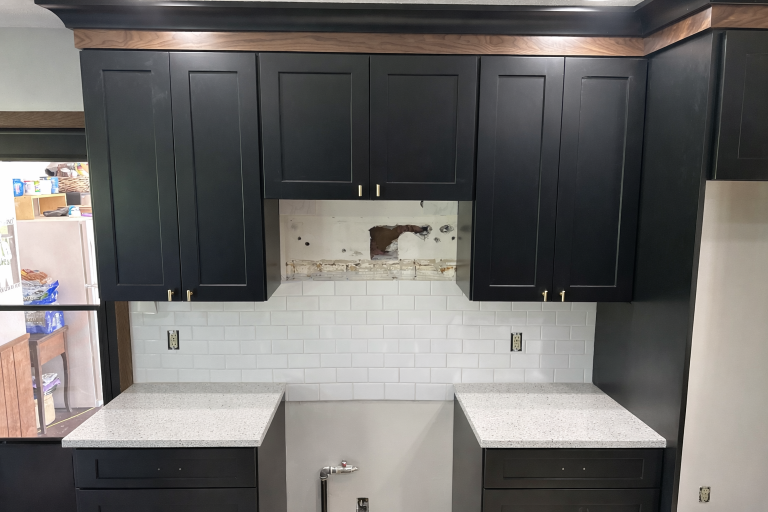 Kitchen cabinets in black with gold handles, white subway tile backsplash, and empty space for stove in the middle, with countertops on each side, and unfinished wall area above the stove space.