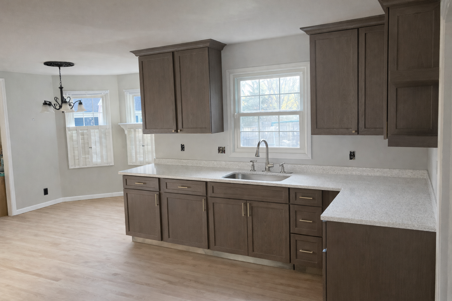 Empty kitchen with wooden cabinets, white speckled countertops, a window above the sink, and light wood flooring.