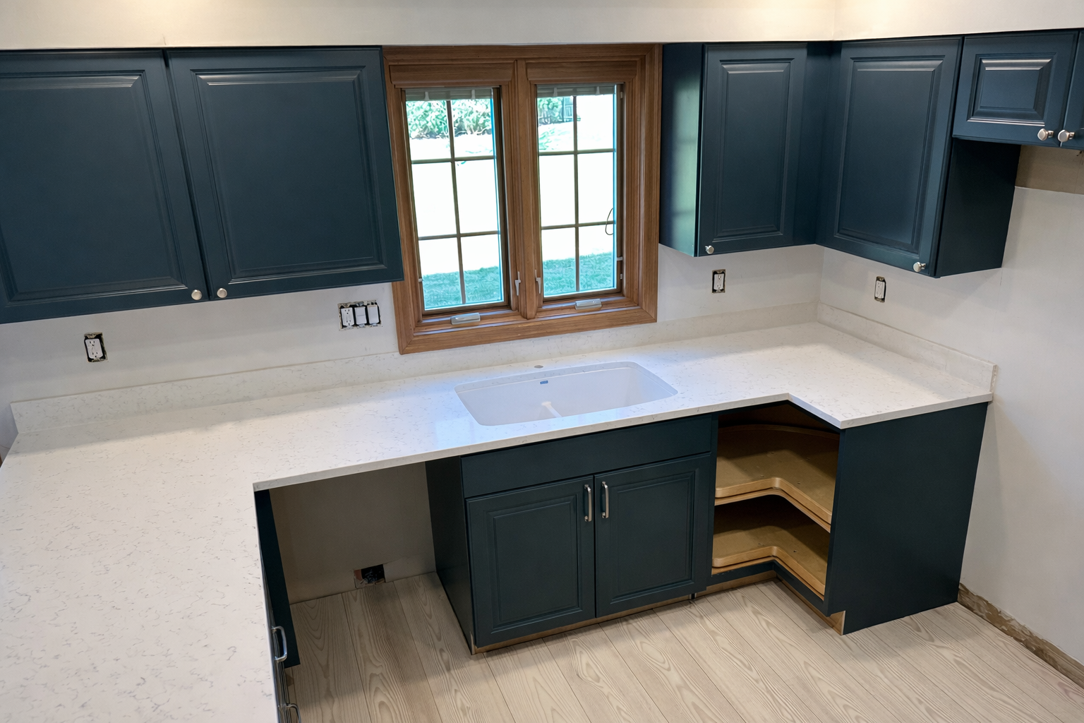 Kitchen with blue cabinets, white countertop, and a double window above the sink, with some cabinet doors missing.
