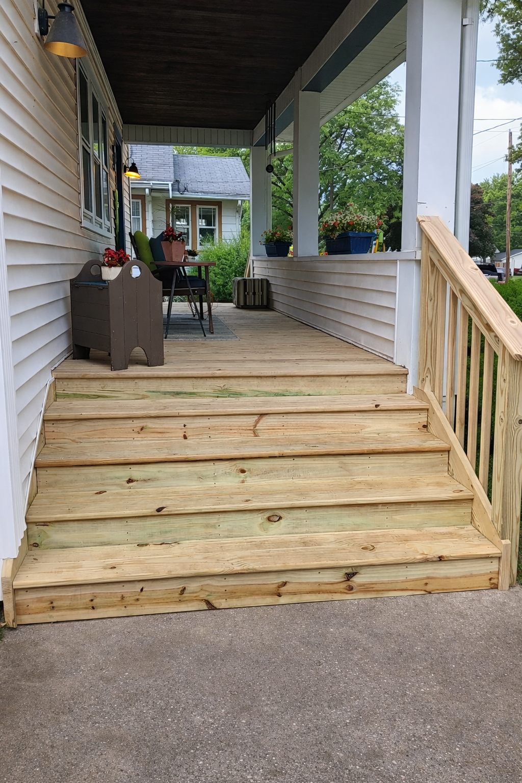 Freshly built wooden front steps leading up to a porch with outdoor furniture and potted plants.