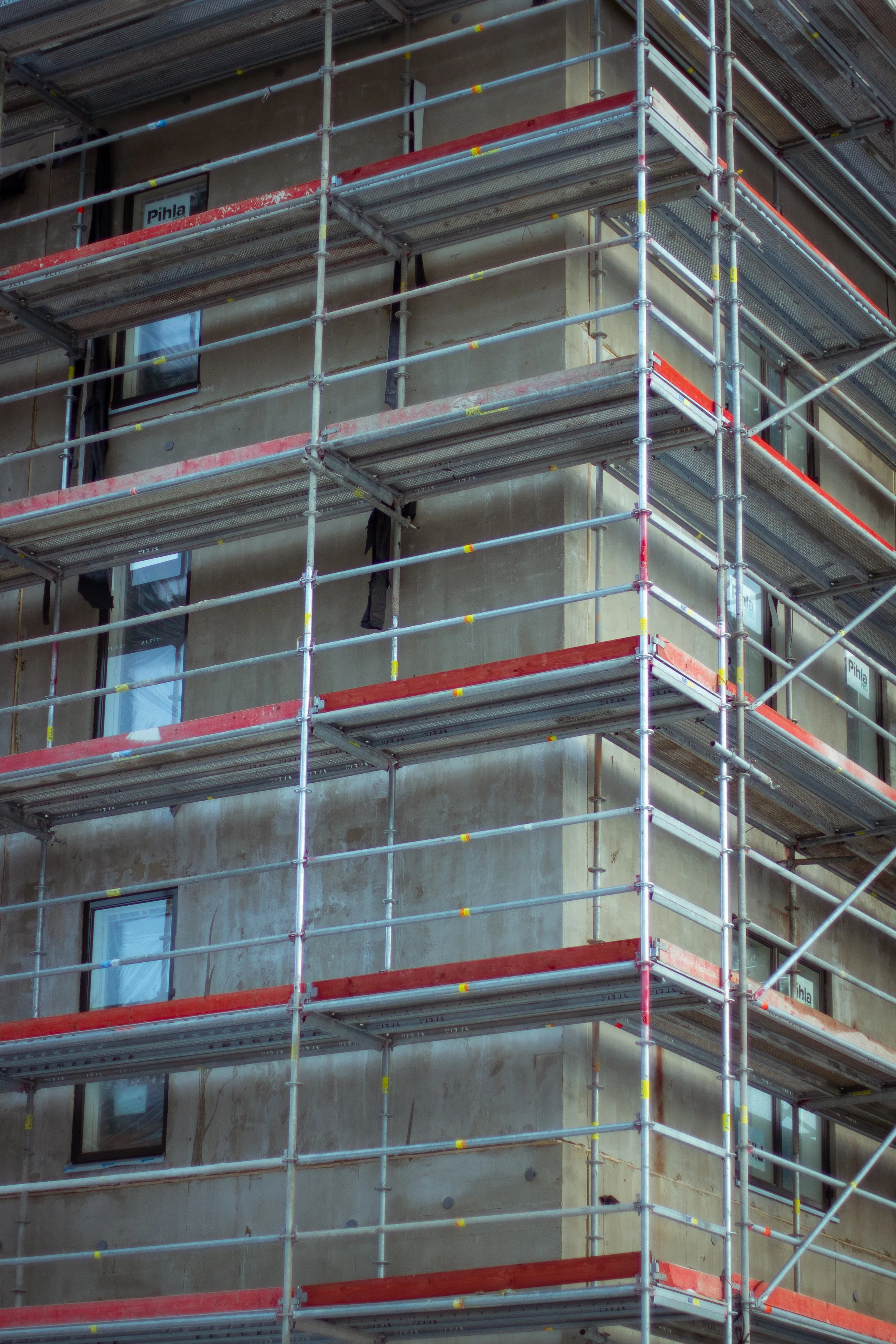 Construction site with scaffolding surrounding a building with unfinished exterior walls and windows.