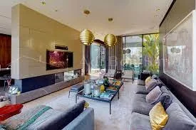 Modern living room with large windows, gray sofas, a glass coffee table, flat-screen TV, and decorative lighting.