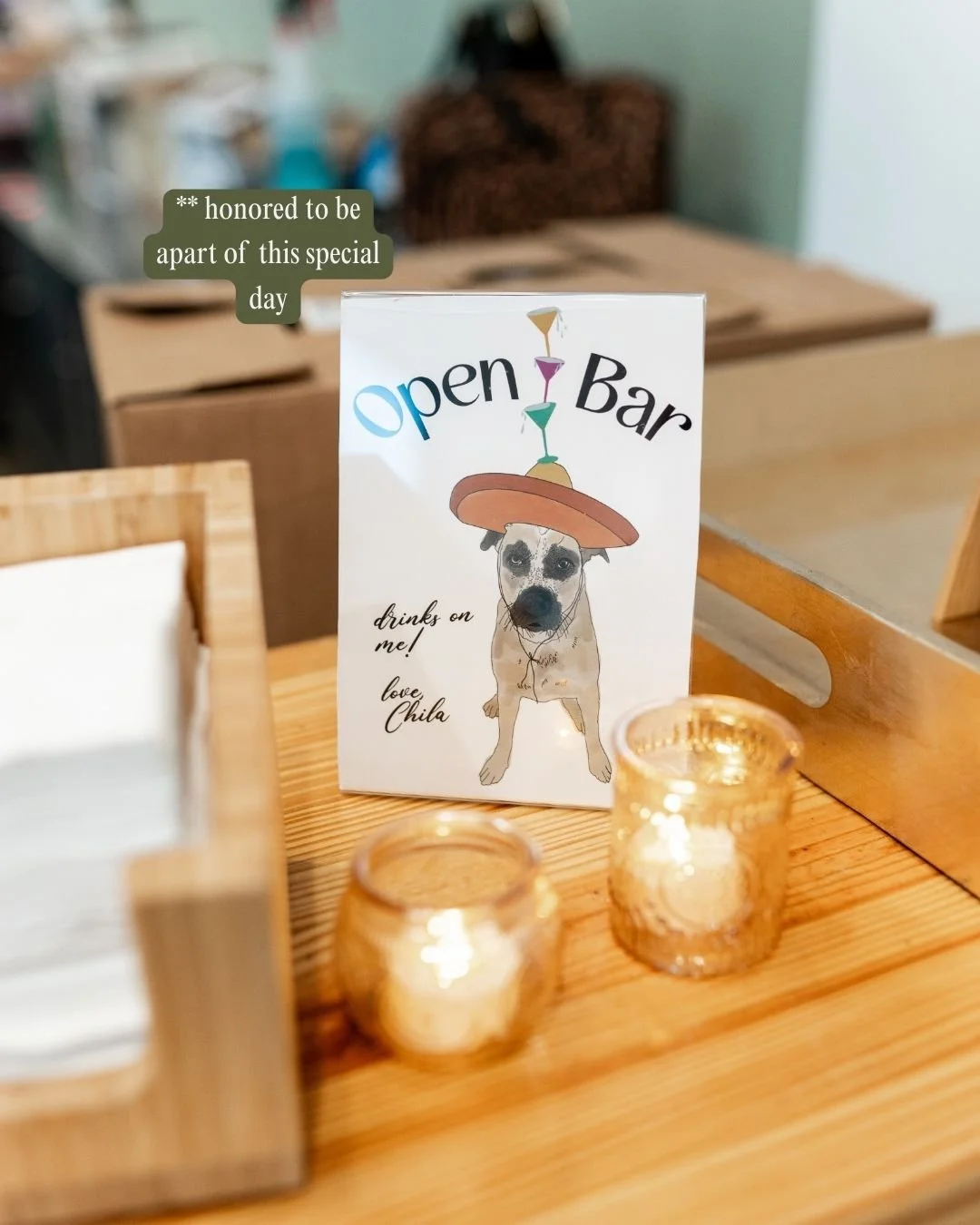 Sign on a table advertising an 'Open Bar' with a dog wearing a sombrero, and candles nearby.