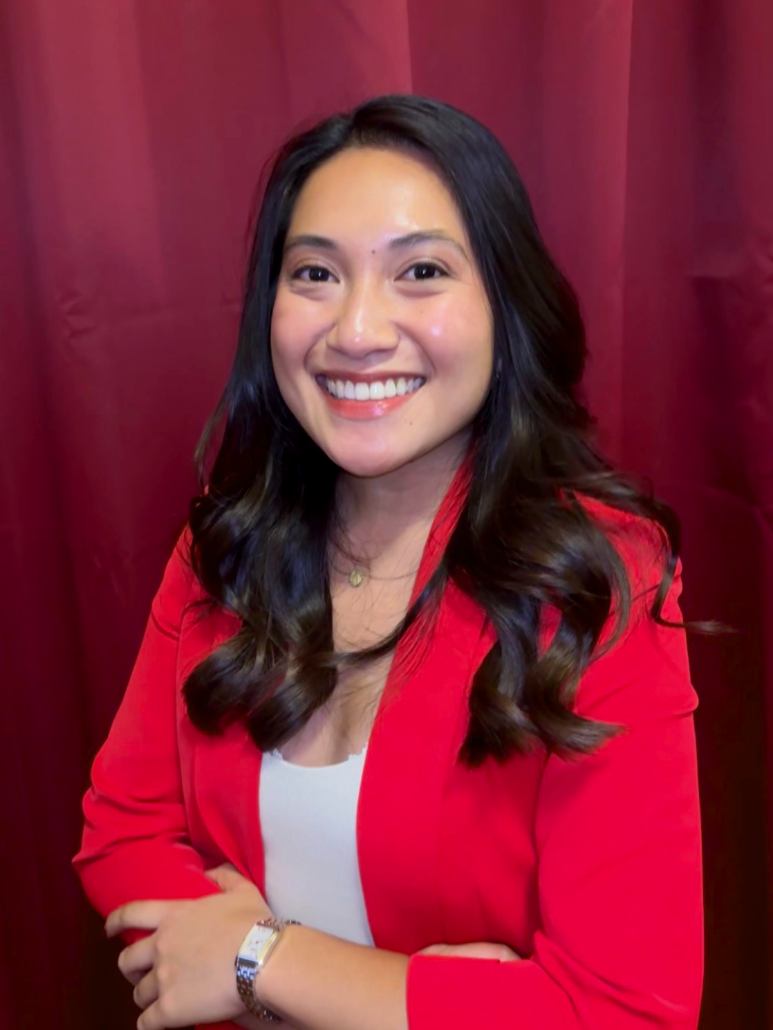 A woman with shoulder-length brown hair smiling in front of a pink and red glittery backdrop.