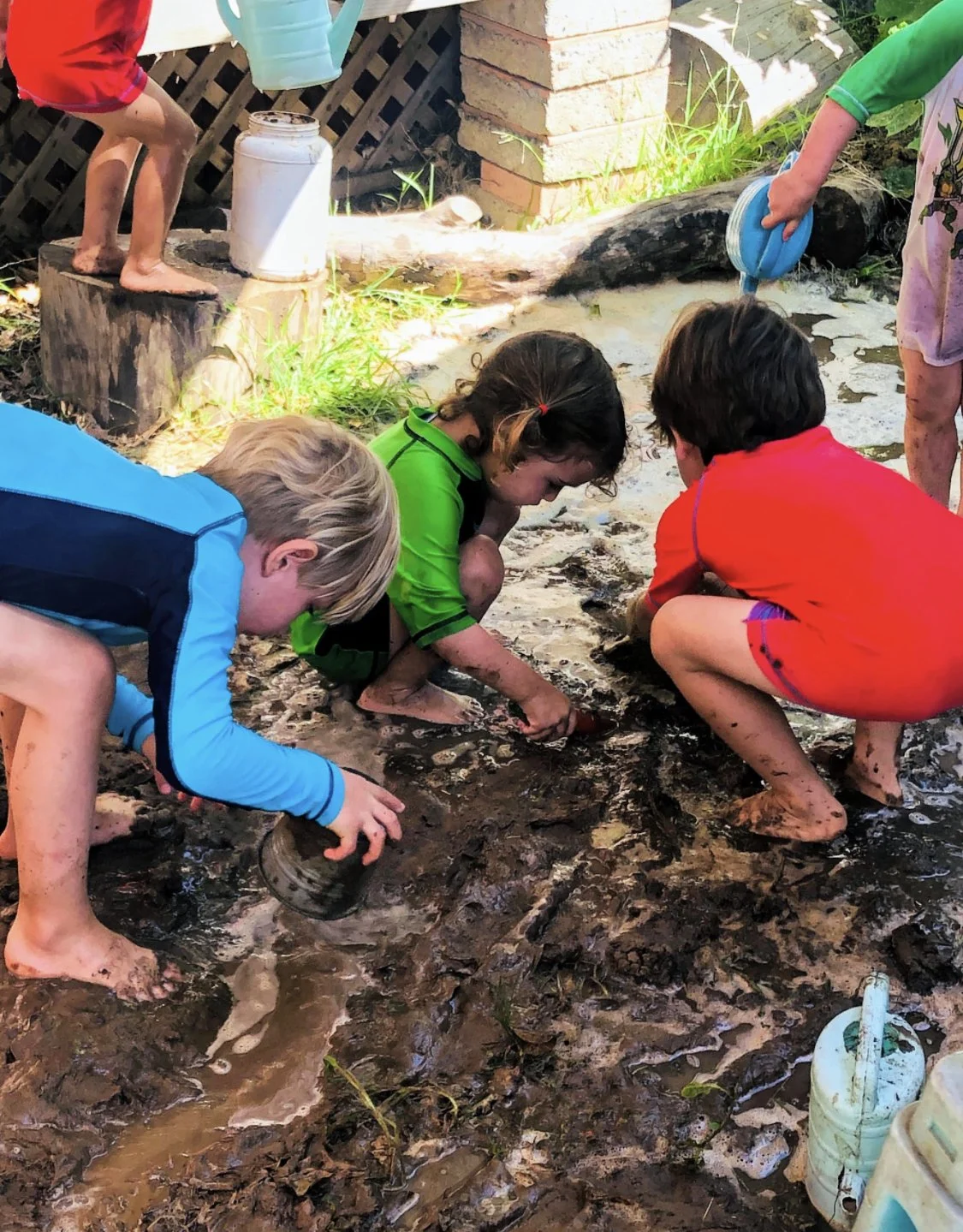 Children playing and digging in muddy water outdoors.
