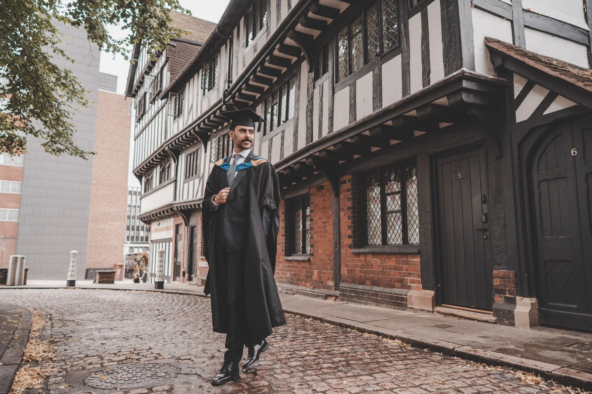 Boy wearing graduation clothes walking through Coventry city centre during a graduation day photo session