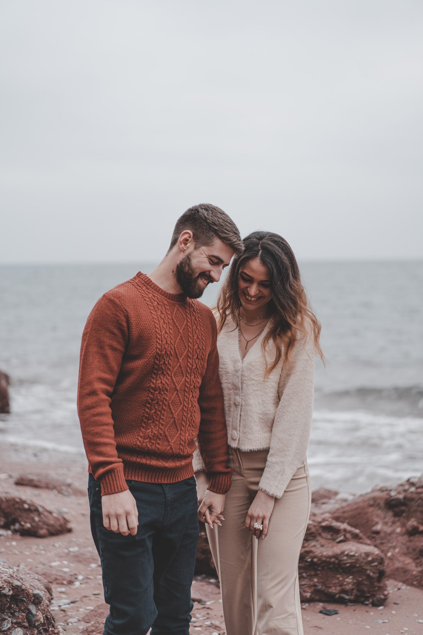 Boy and girl holding hands and laughing on a beach in Torquay