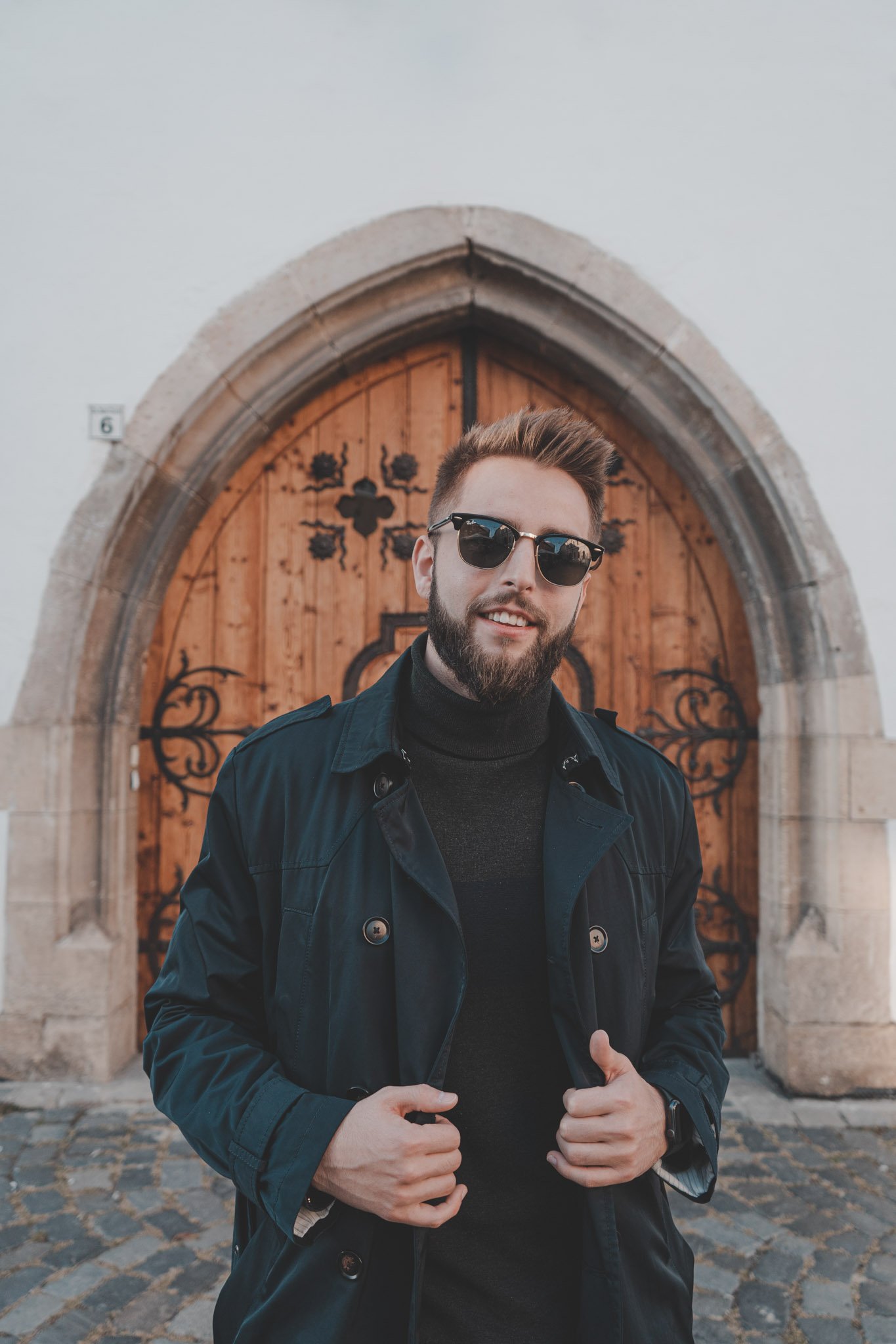 Young man looking at the camera in front of an old wooden gate in Cluj-Napoca