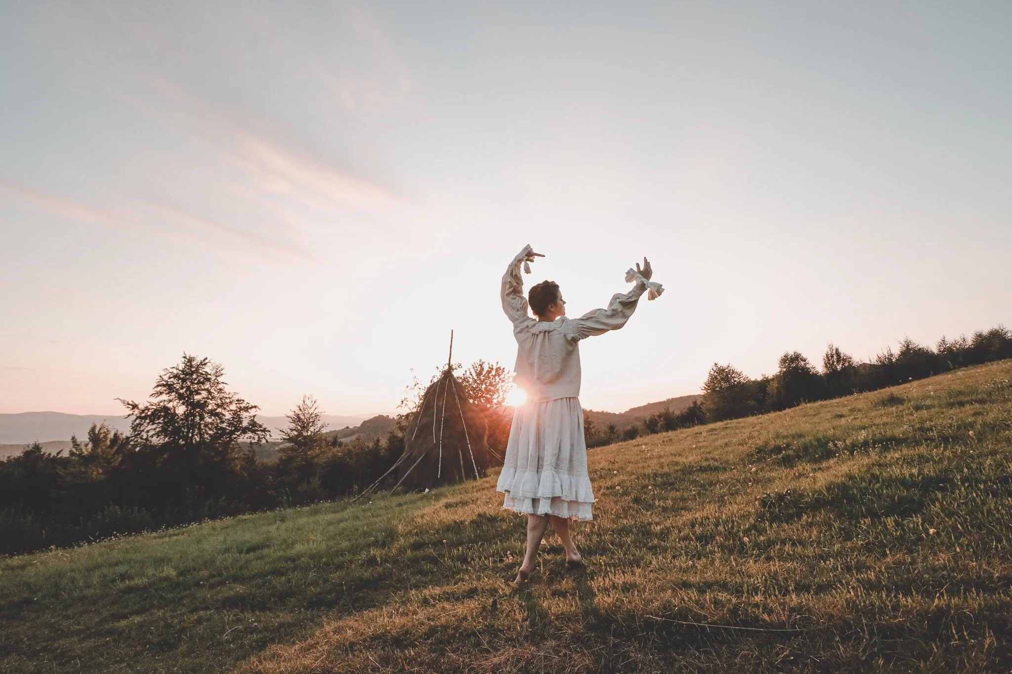 Young woman wearing romanian traditional clothes dancing while the sun sets on a field