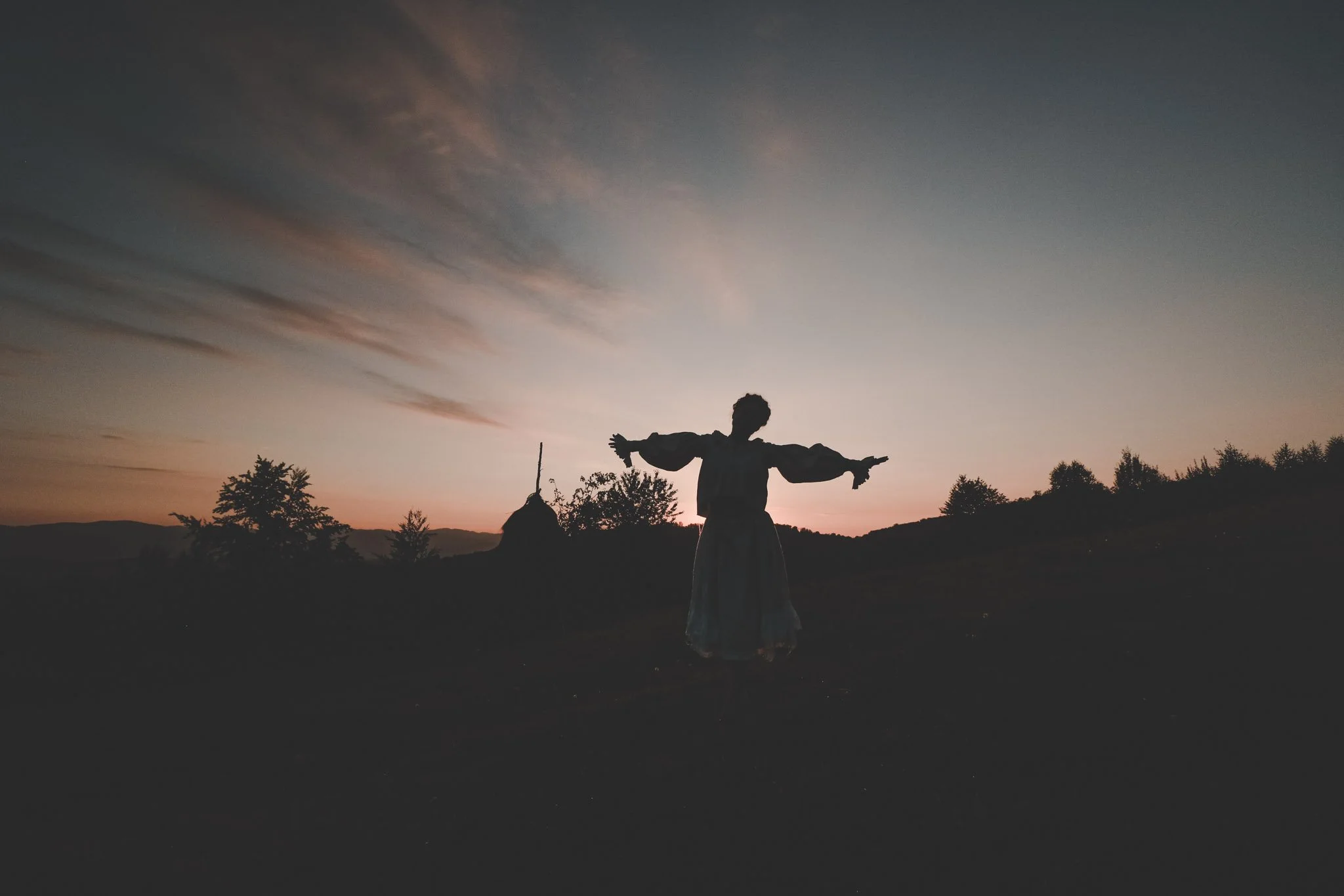 Contre-jour photo of a young woman dancing on a field while the sun sets