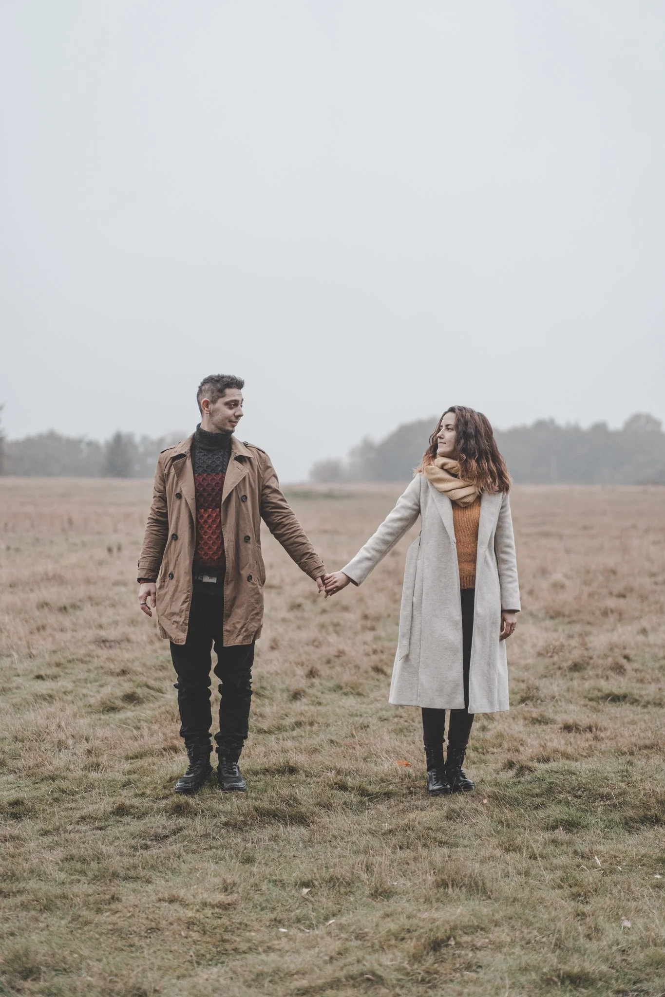 Boyfriend and girlfriend holding hands and watching each other, facing the camera, on a field at Coombe Abbey Park, Coventry