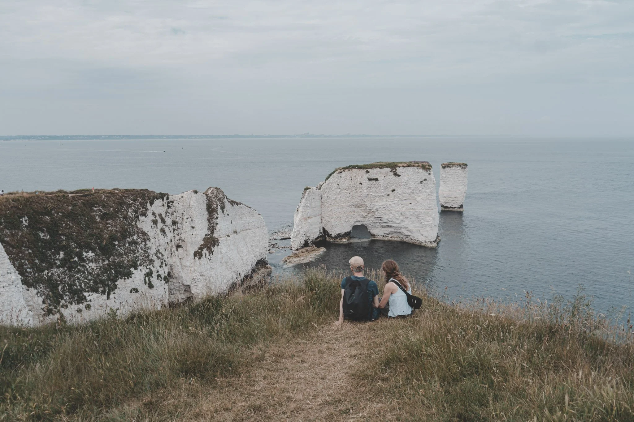 Man and woman sitting on the edge of Old Harry Rocks in Dorset, United Kingdom