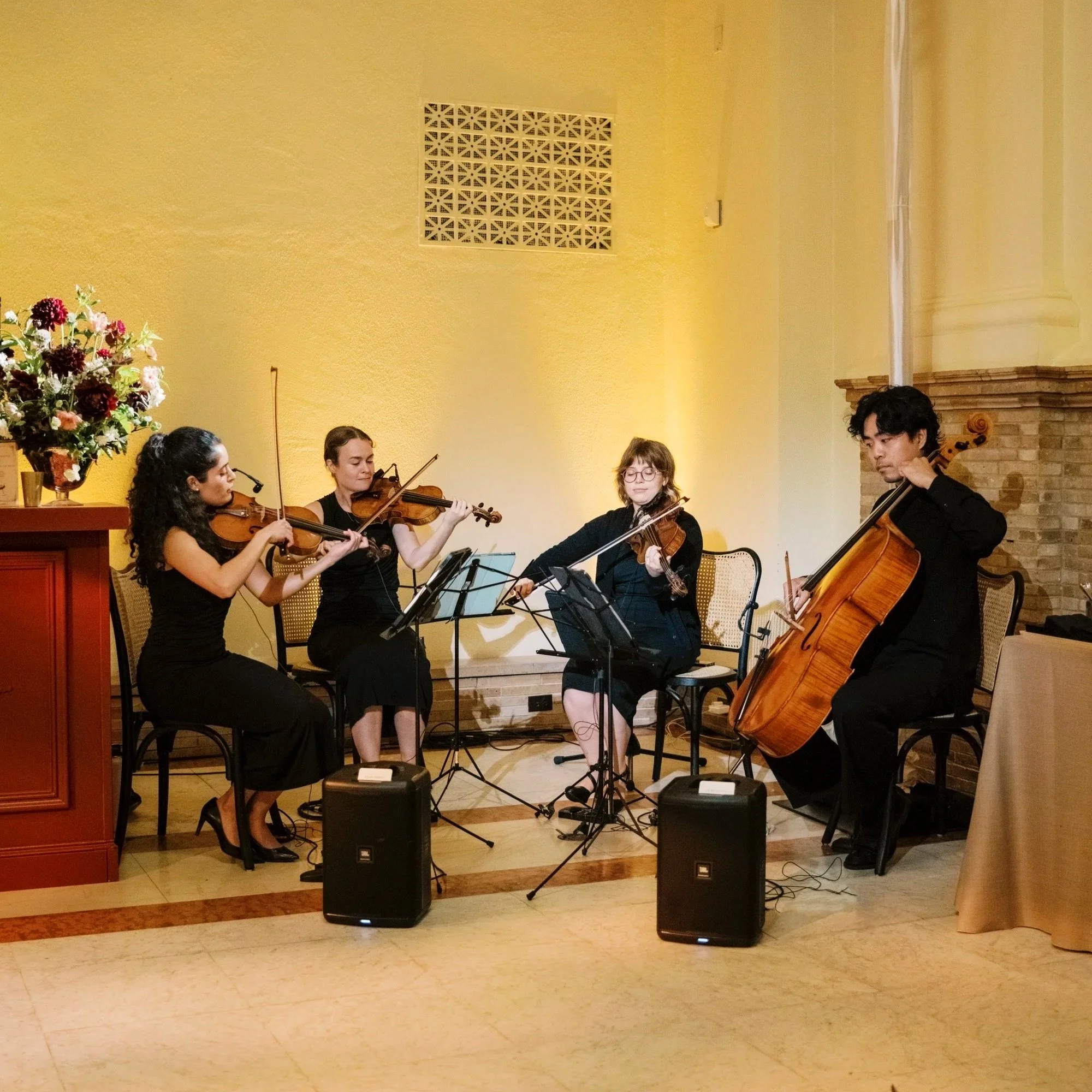 Four musicians playing amplified string instruments in the Boston Public Library.