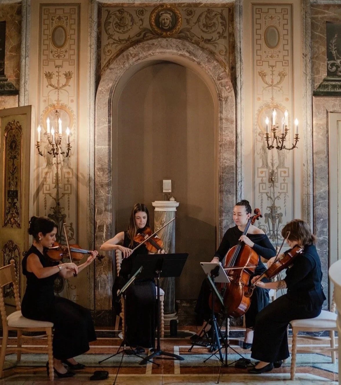 String Quartet playing string instruments in the Brandegee Estate: an elegant, ornate, historic room with gold and marble decor and chandeliers.
