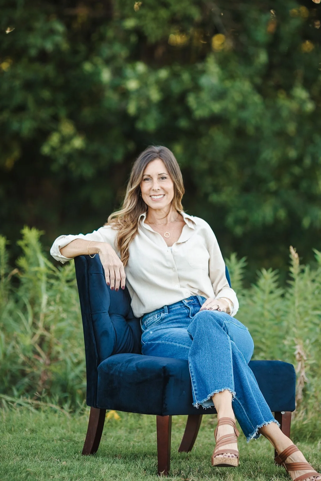 Health coach smiling while seated outdoors surrounded by greenery.