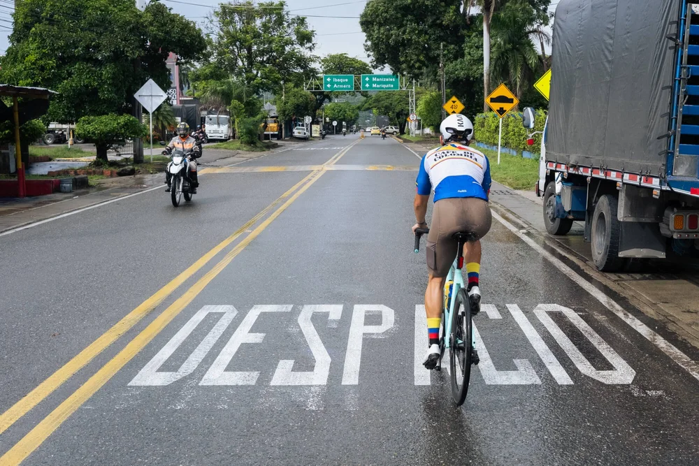A cyclist on a wet mountain road marked DESPACIO, Into Coffee Heartlands