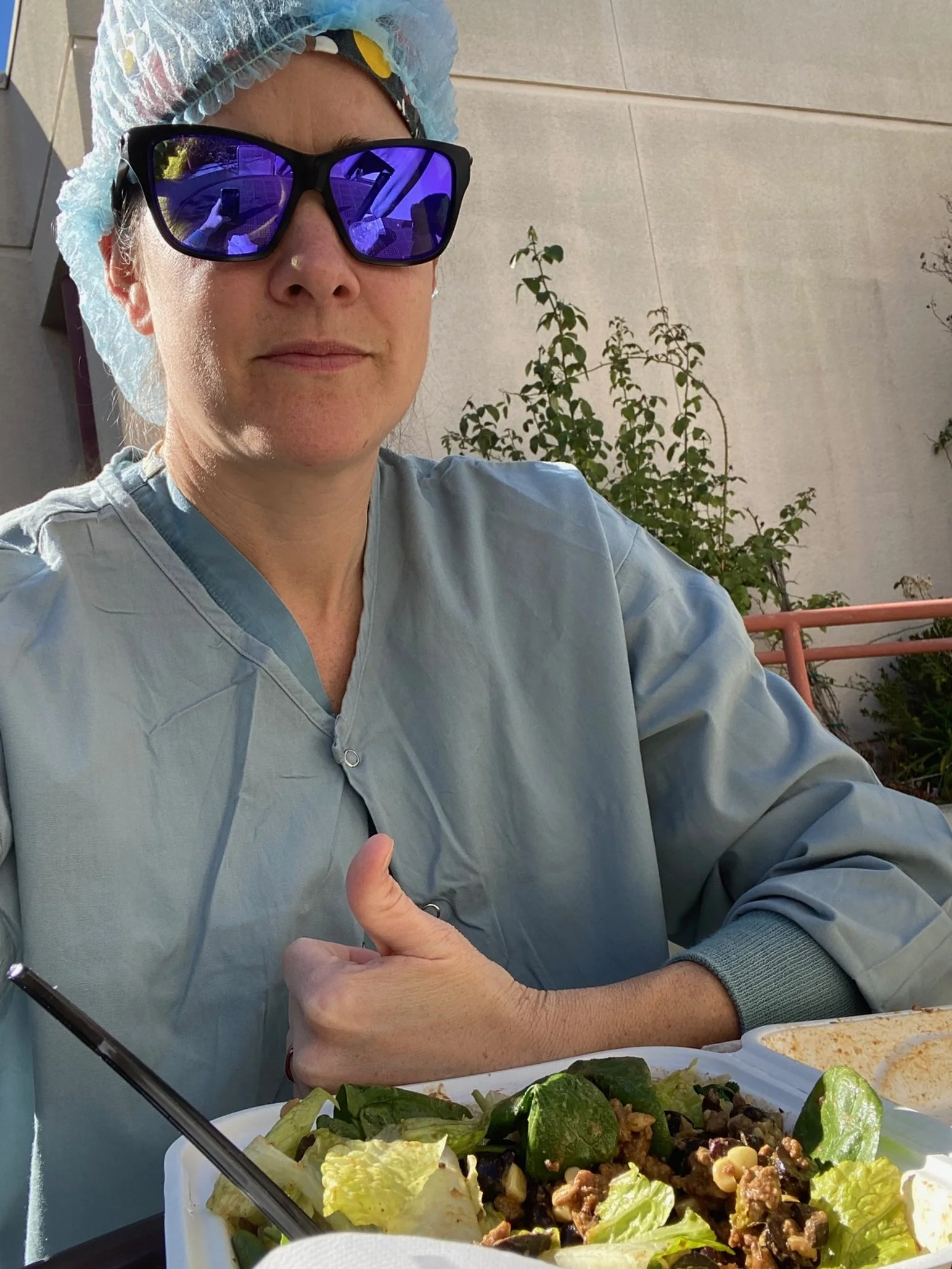 blog author Sarah in scrubs and sunglasses eating a salad at the hospital on her break