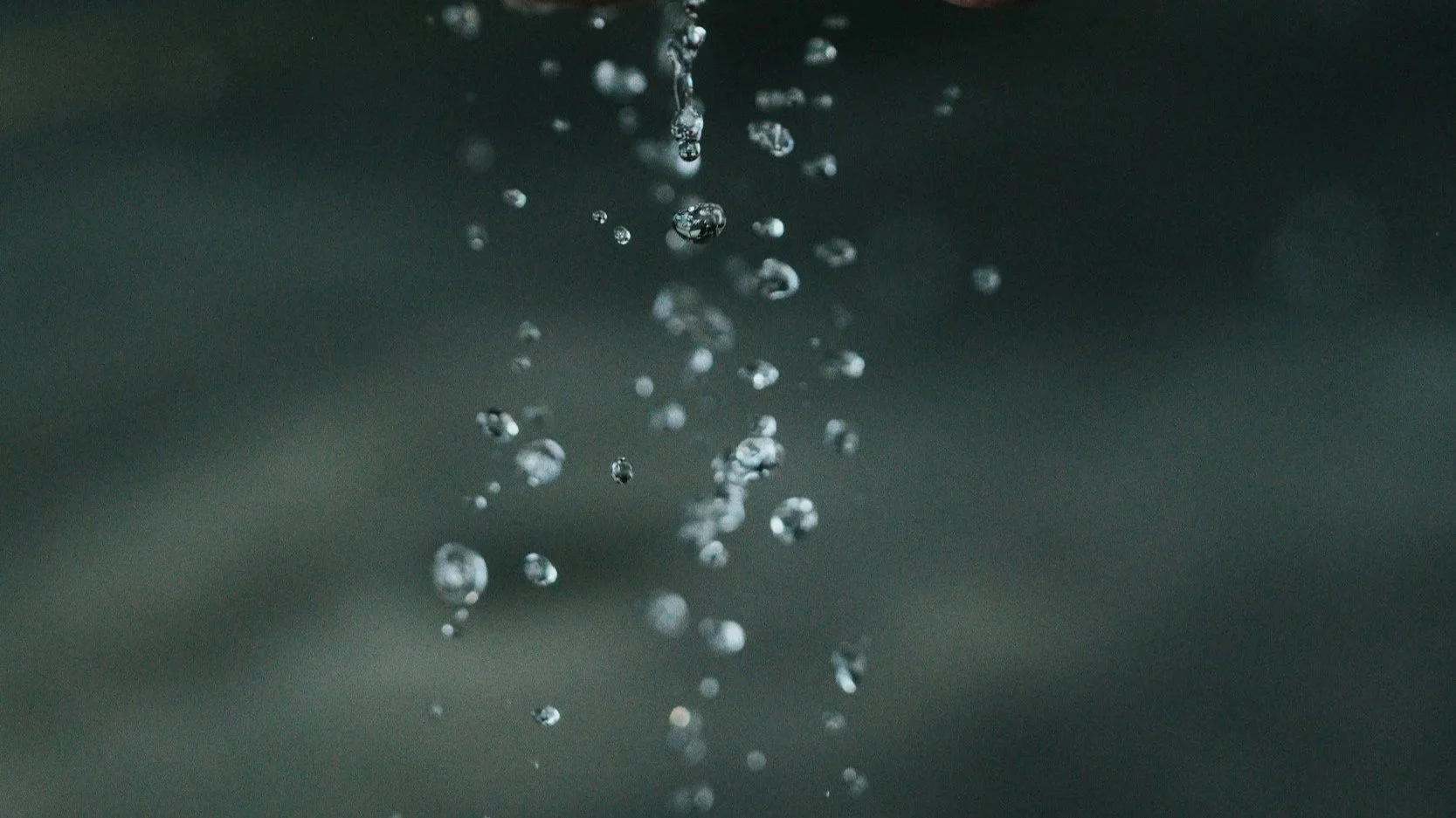 Close-up of water droplets falling through the air against a dark background.