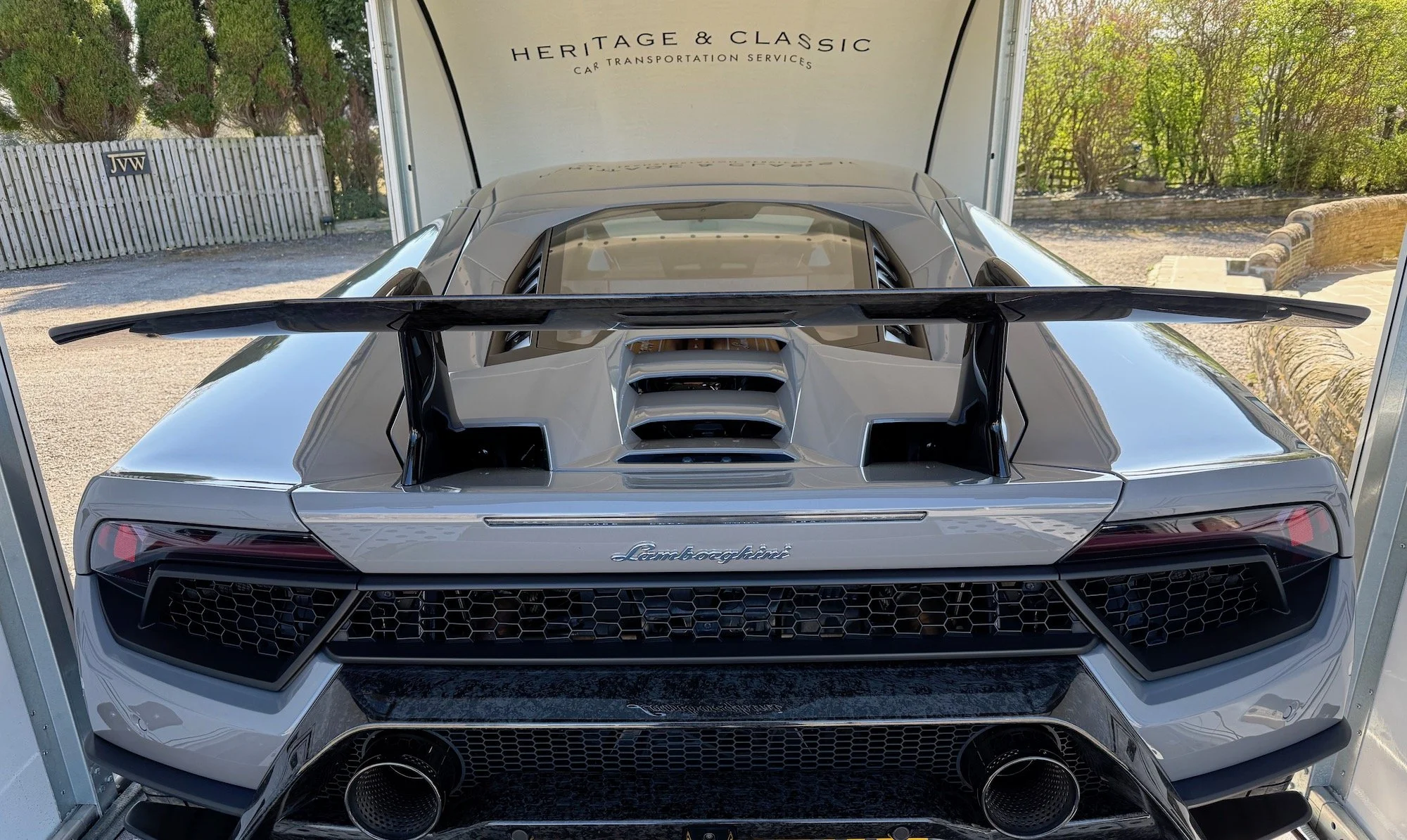 Silver Lamboghini inside a trailer with Heritage & Classic Car Transportation branding, offering services like vehicle inspection, tracking, and insurance.