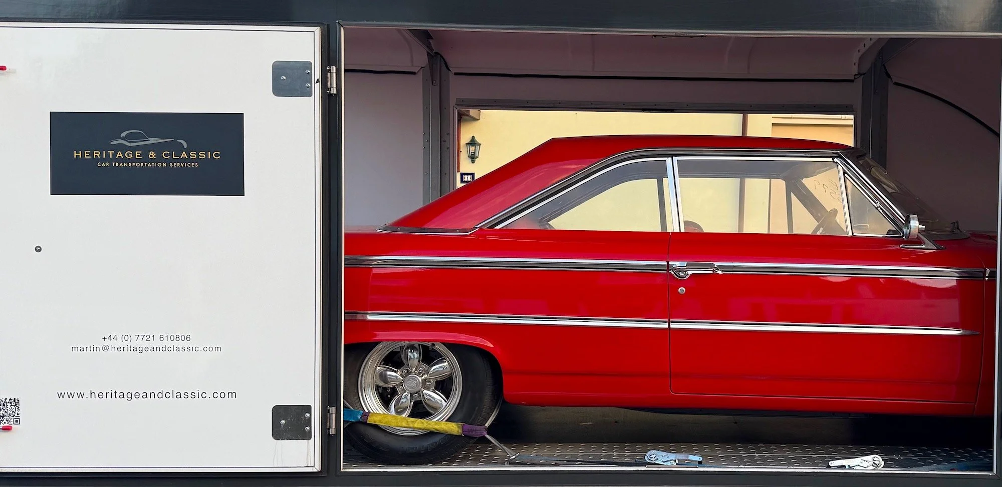 Red Ford Galaxy inside a trailer with Heritage & Classic Car Transportation branding, offering services like vehicle inspection, tracking, and insurance.