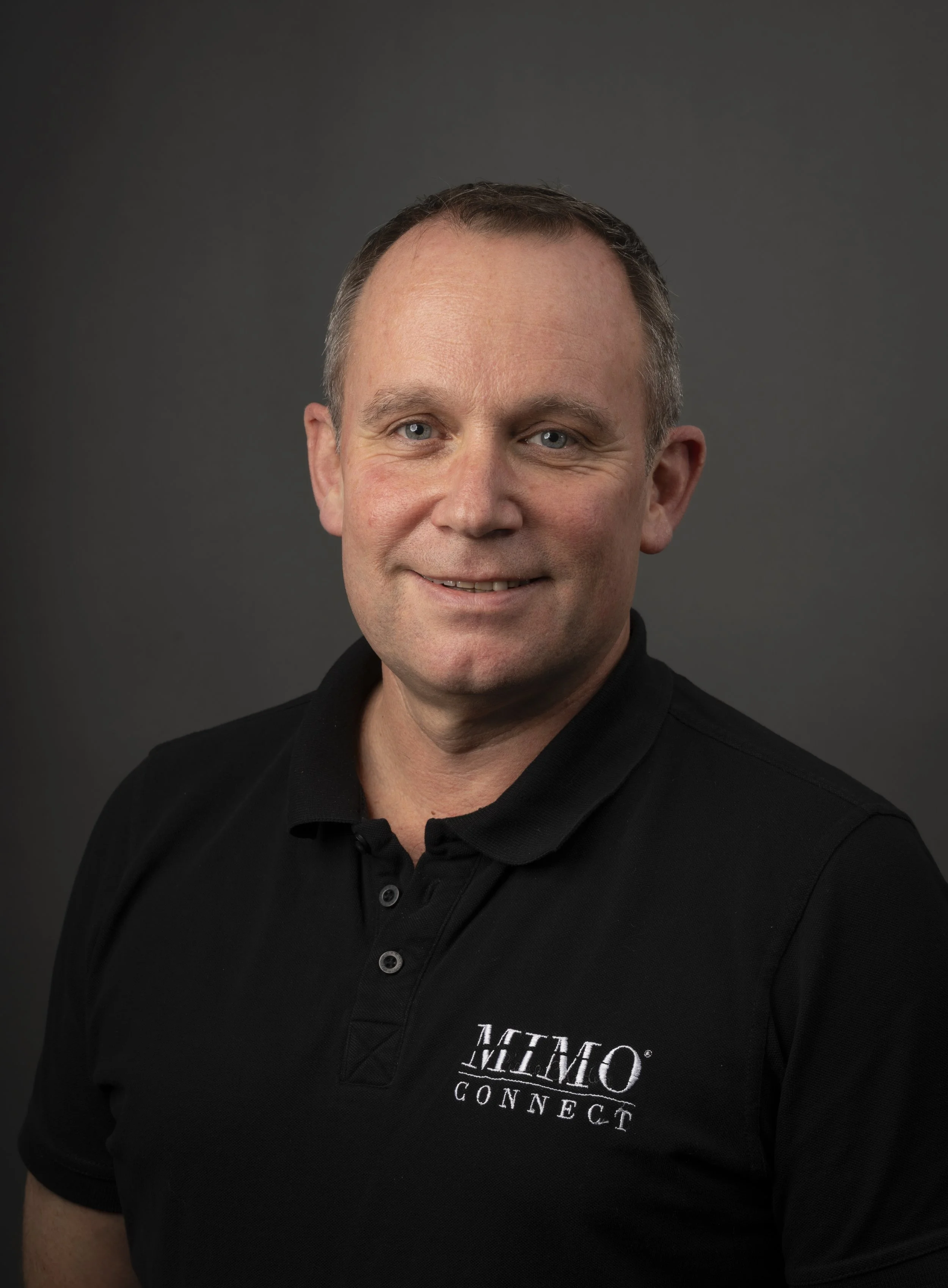 A smiling man in a black shirt with the white logo 'MIMO CONNECT' against a dark gray background.