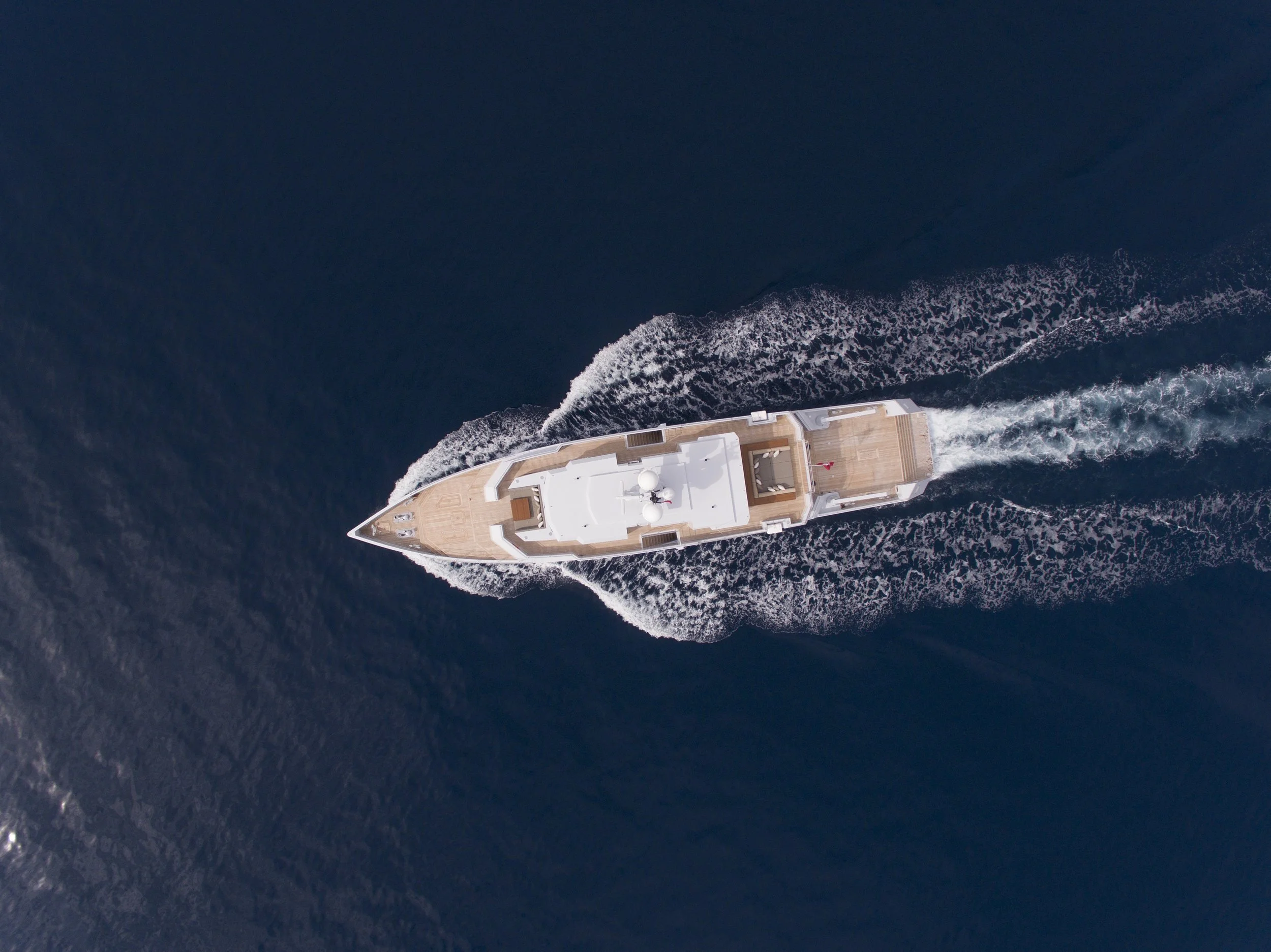 Aerial view of a white yacht cruising through deep blue ocean water, creating a wake behind it.