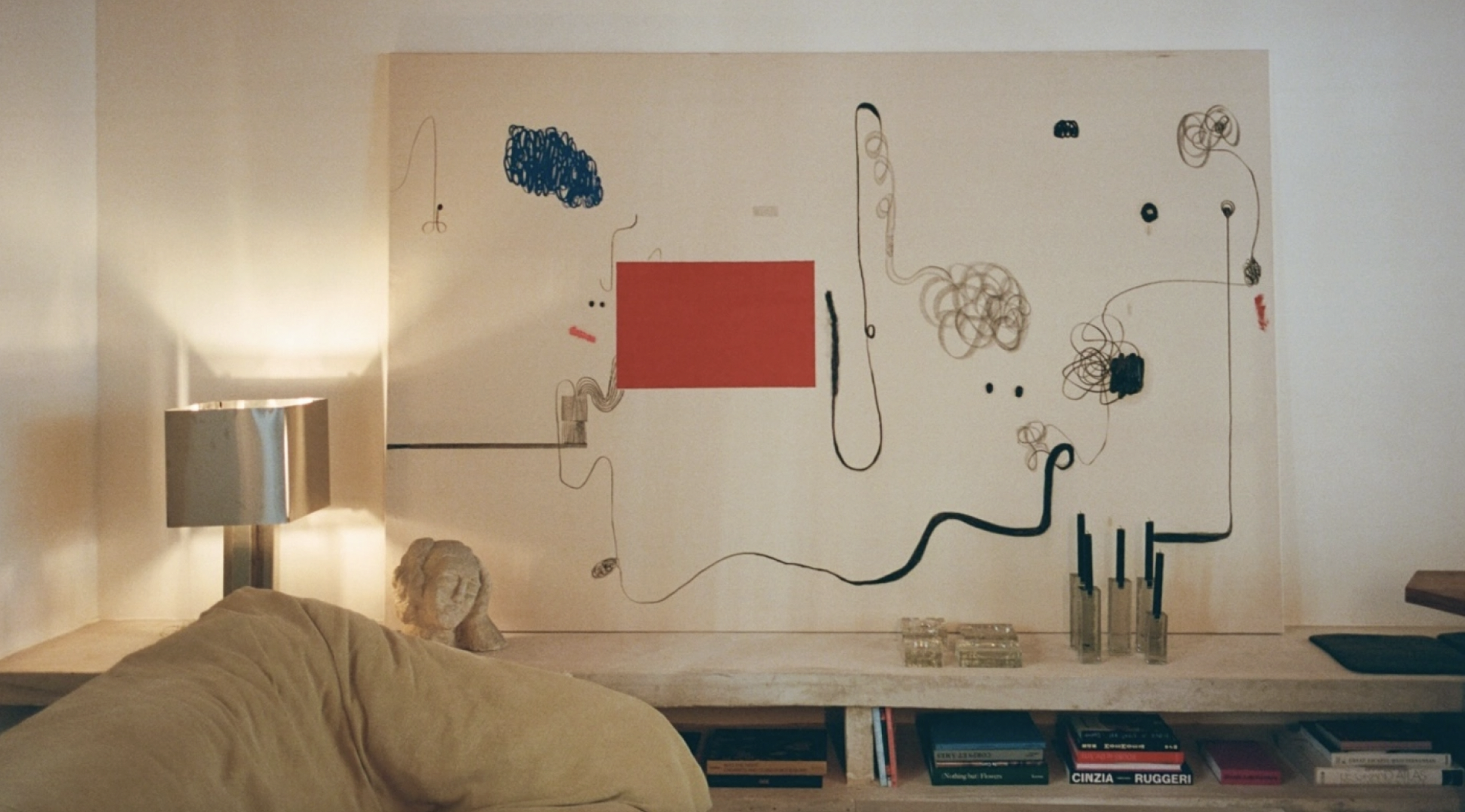 Living room with beige sofa, metallic table lamp, abstract wall art, and bookshelf with books.