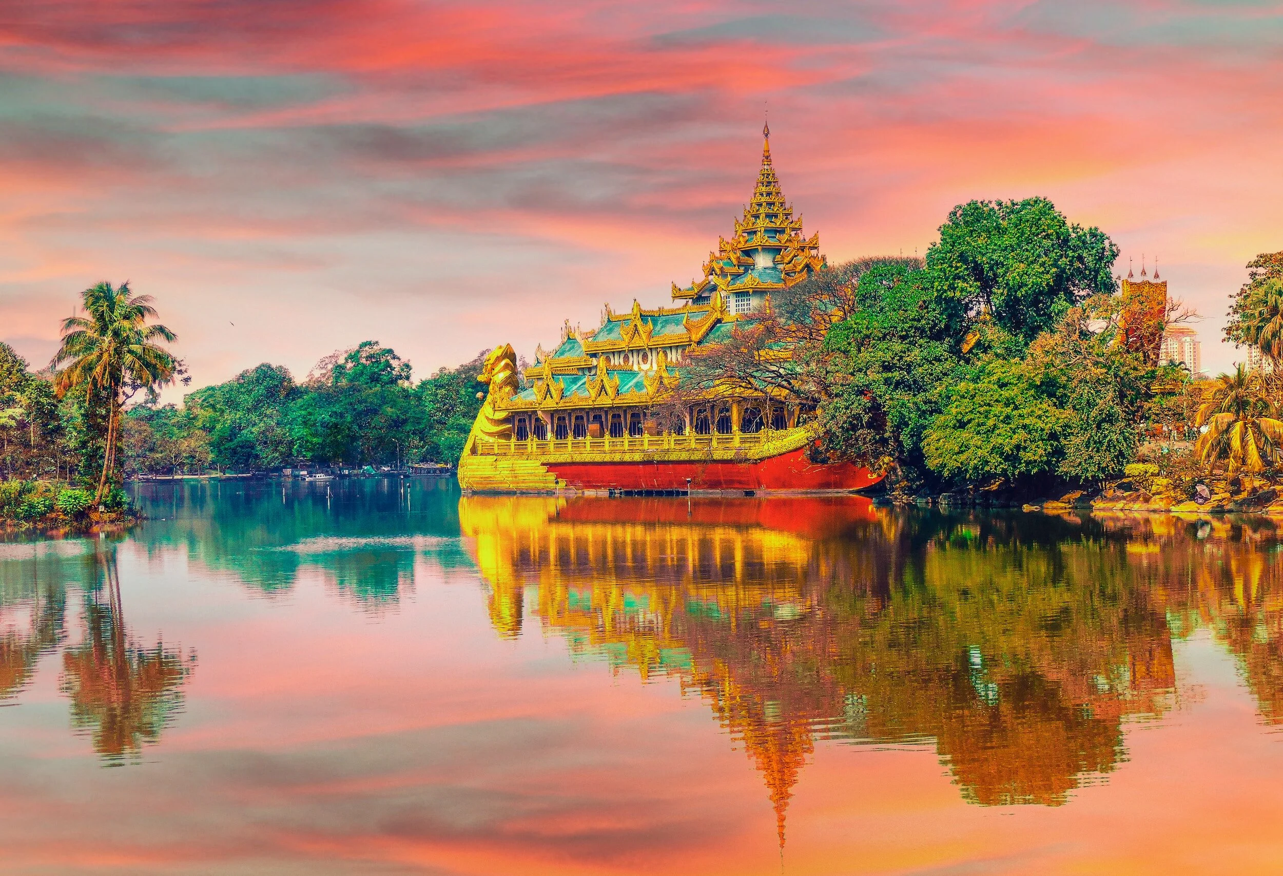 A traditional ornate boat rooted on the edge of a river, surrounded by trees and reflections on the water during a colorful sunset sky.