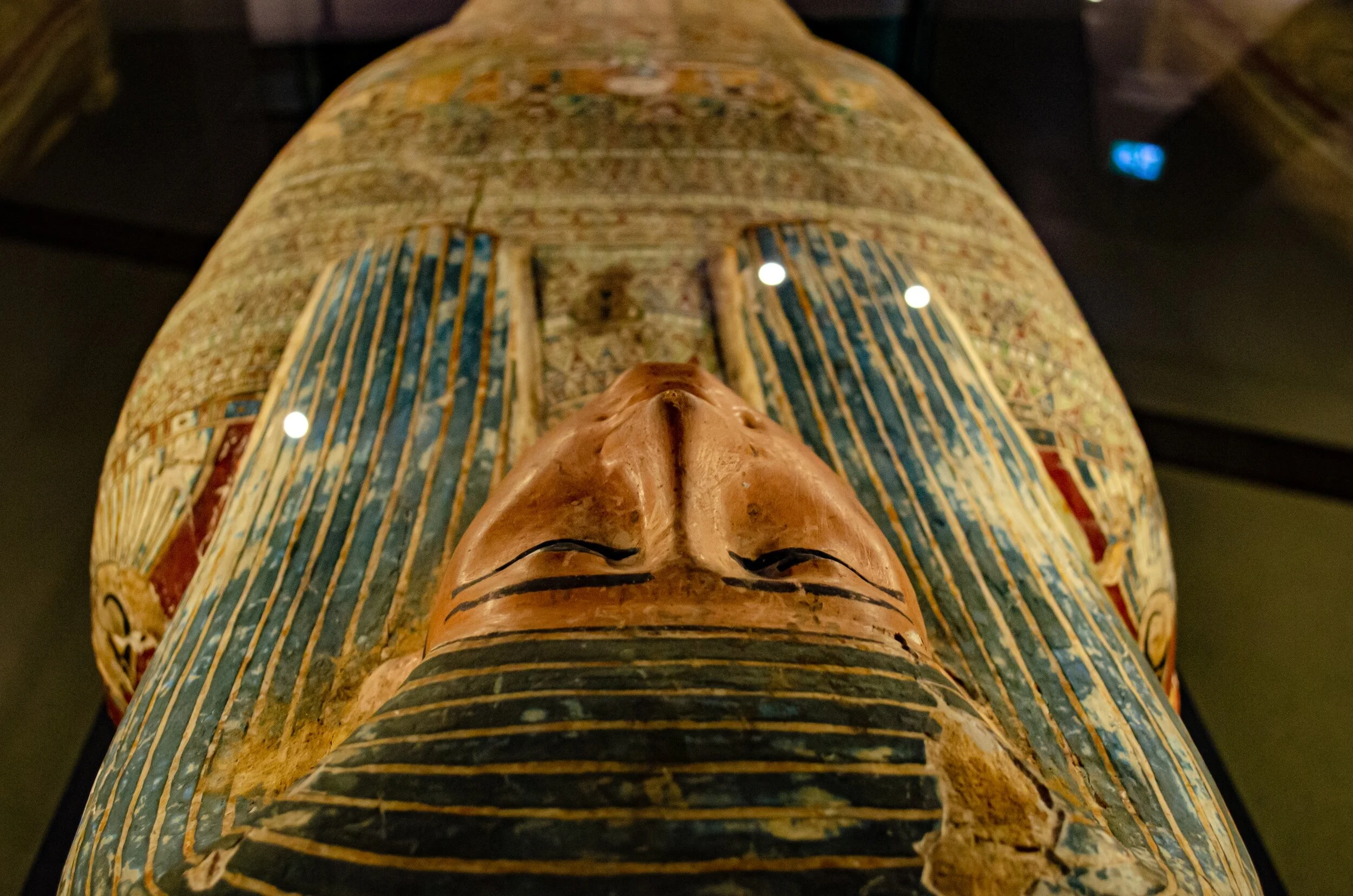 Ancient Egyptian painted wooden funerary mask with detailed face and headdress, displayed in a museum.