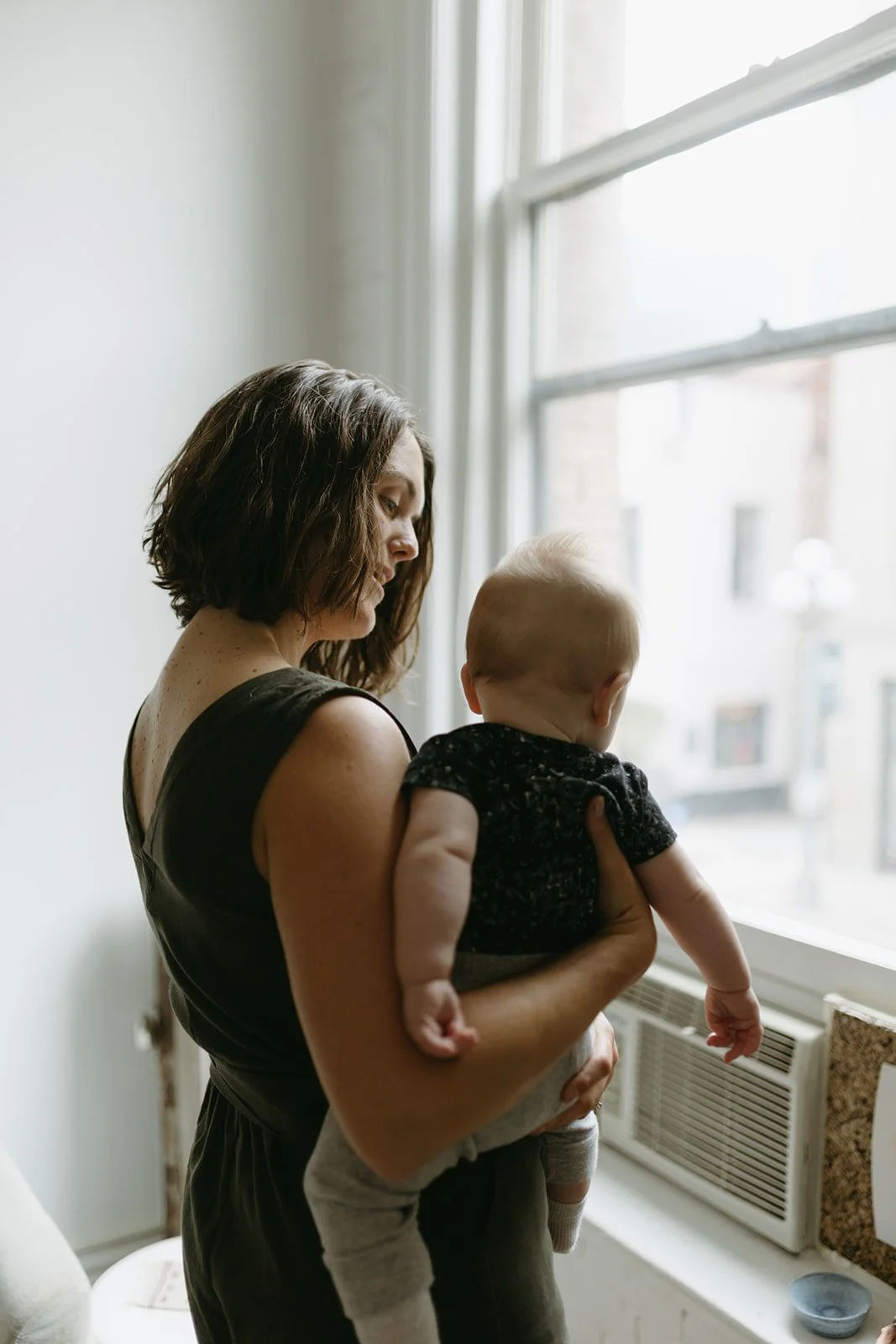 A mother smiling as she holds her baby by a bright window