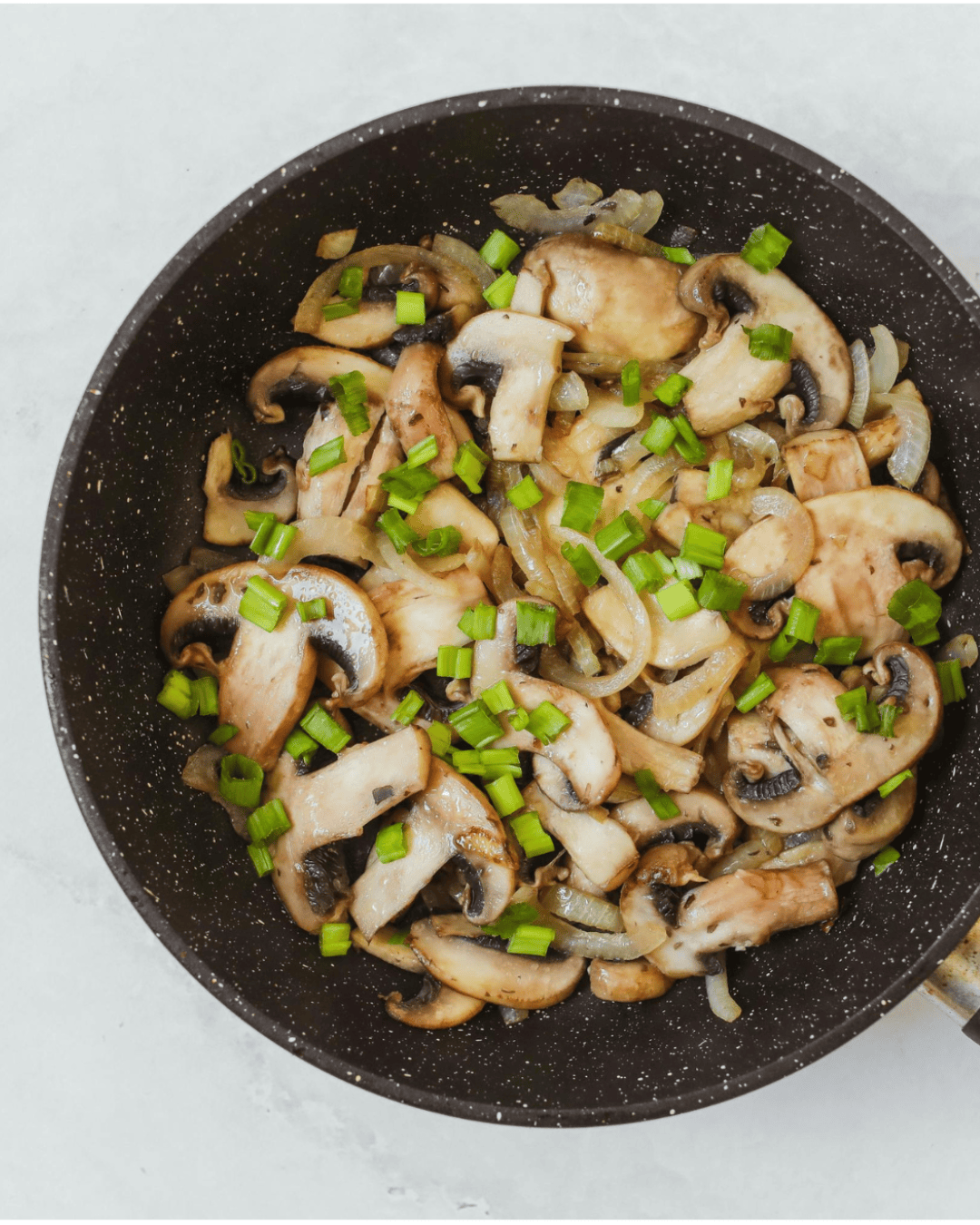 Poêlée chaude de champignons dorés et oignons fondants, avec cébettes fraîches sur le dessus, servie dans une assiette rustique