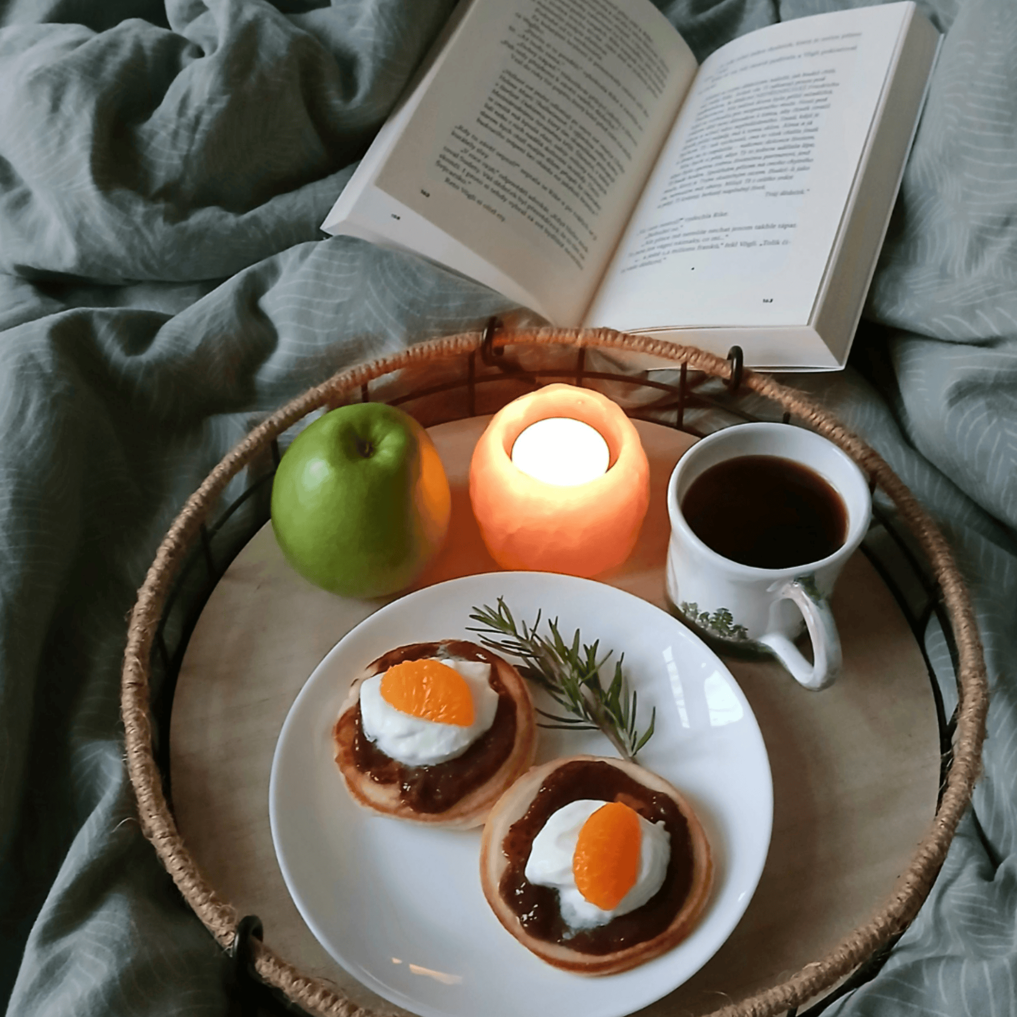 Petit-déjeuner composé de mini pancakes garnis de fromage blanc, compote et quartiers de clémentine, servis sur un plateau avec café, bougie et pomme