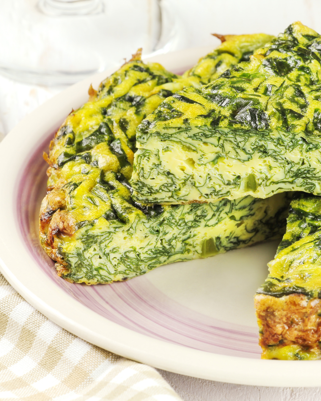 Part de frittata aux épinards et oignons nouveaux servie sur une assiette blanche