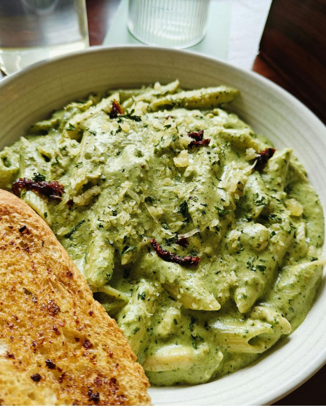 Assiette de pâtes nappées d’une crème verte aux épinards, servie avec croûtons dorés, copeaux de parmesan et herbes fraîches