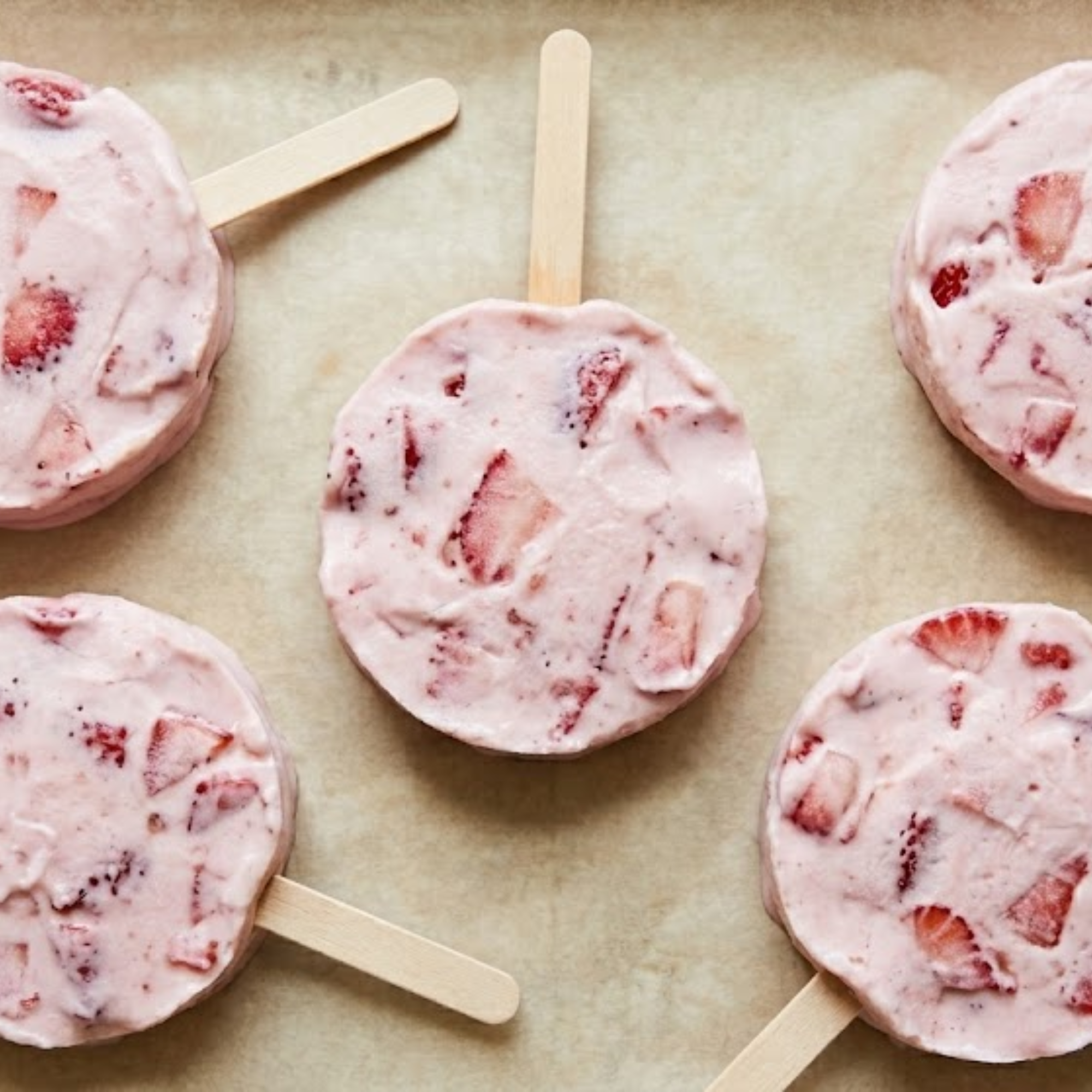Palets glacés maison aux fraises, yaourt grec et fromage blanc, servis sur bâtonnets en bois.