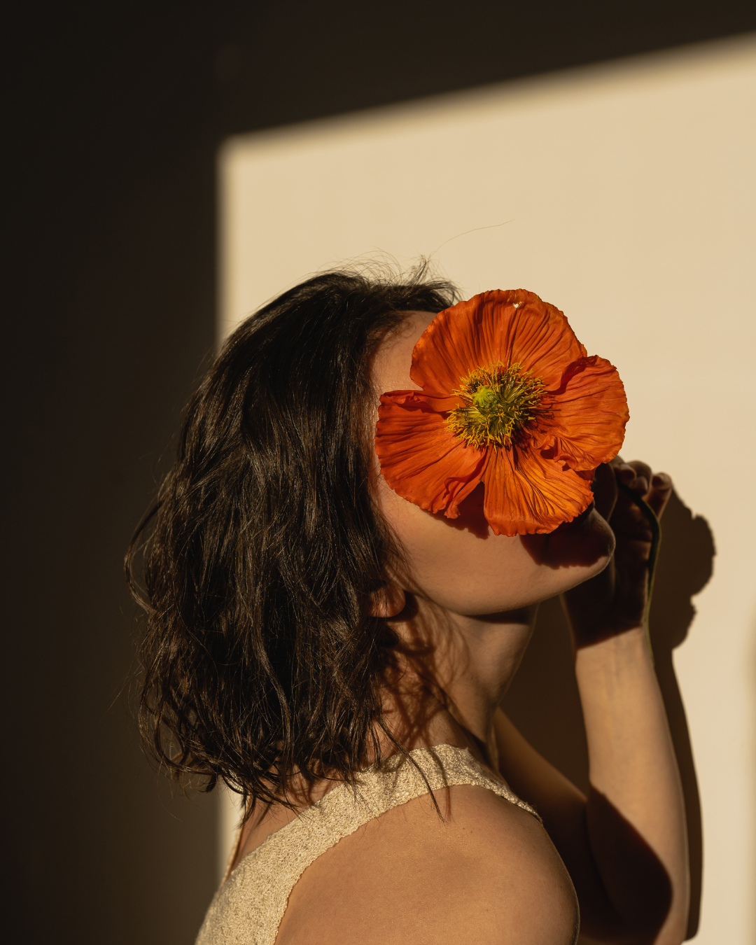 Femme avec un gros coquelicot orange couvrant son visage, dans une lumière chaude.