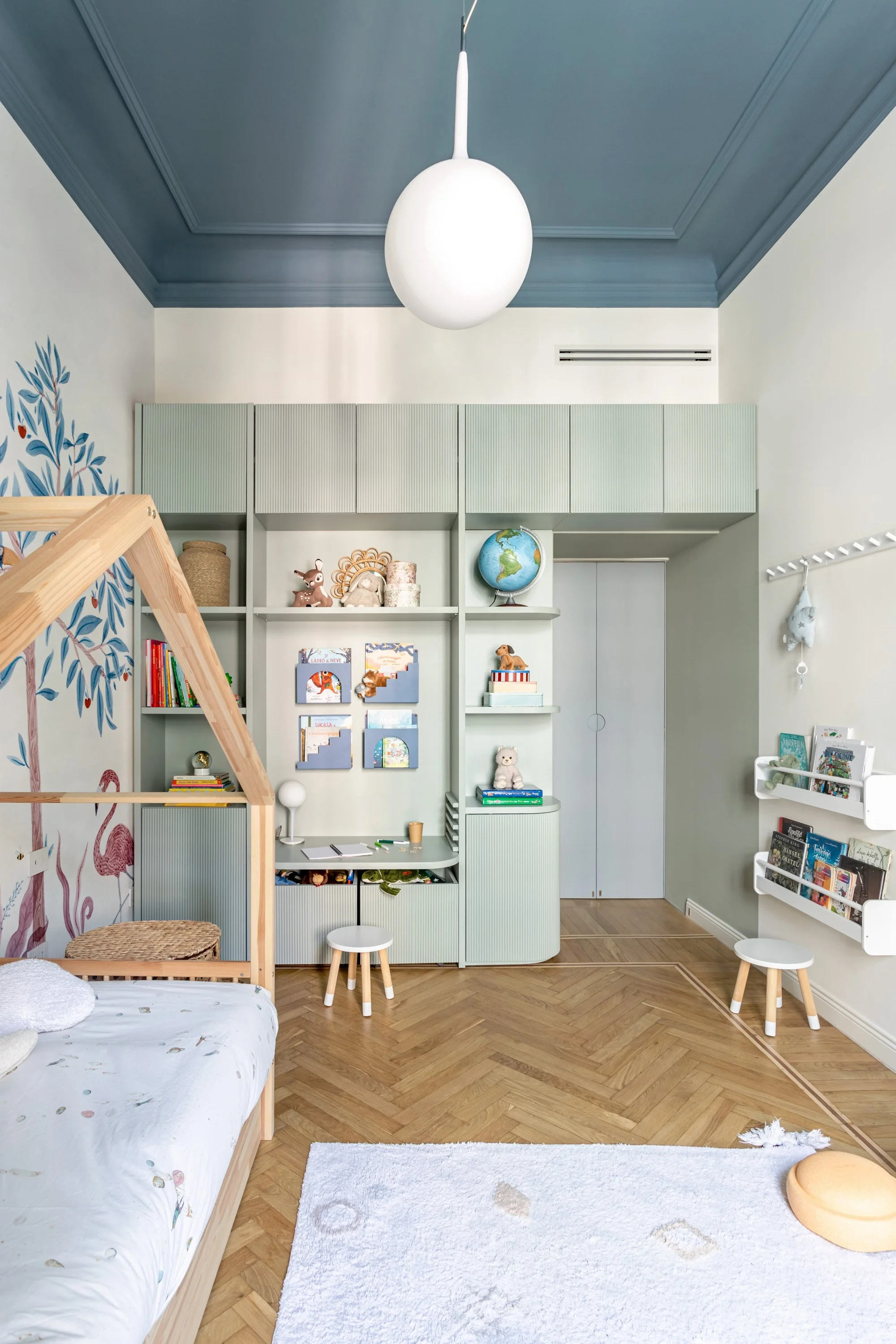 Camera per bambini con letto a casetta, carta da parati illustrata e parete attrezzata su misura.