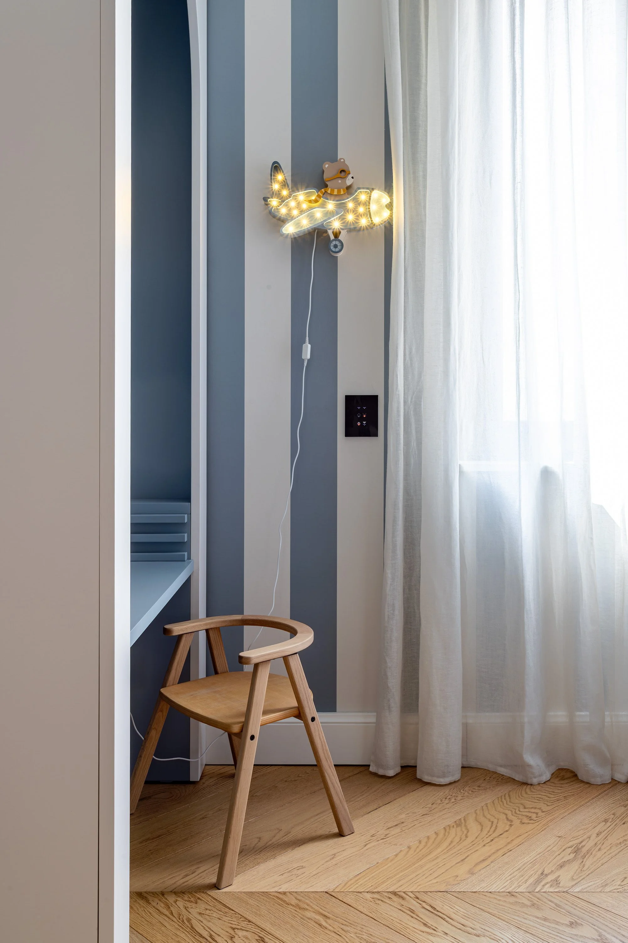 Angolo della camera con parete a righe blu, seduta e applique decorativa.