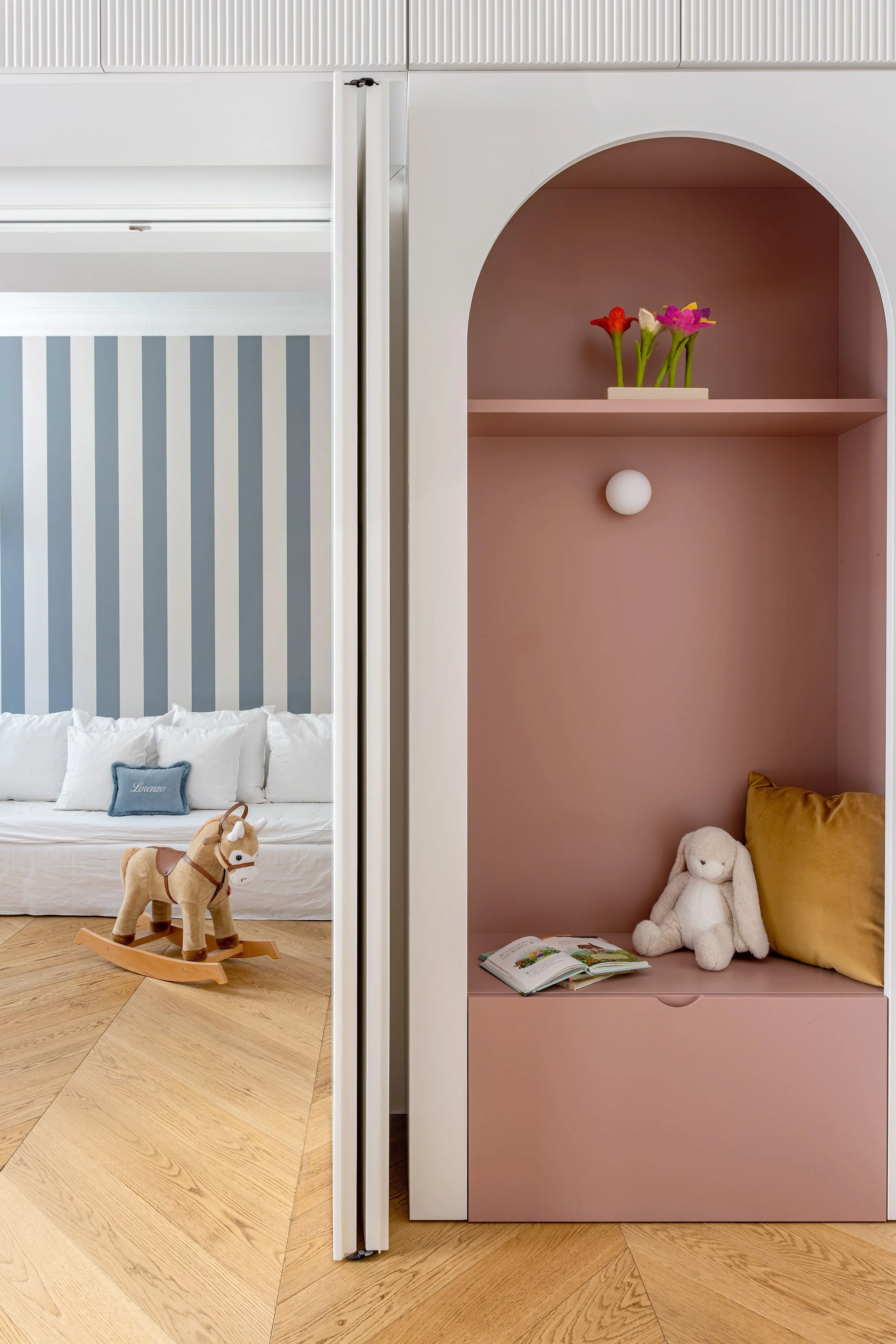 Nicchia rosa per lettura e relax, affacciata sulla camera adiacente con parete a righe blu.