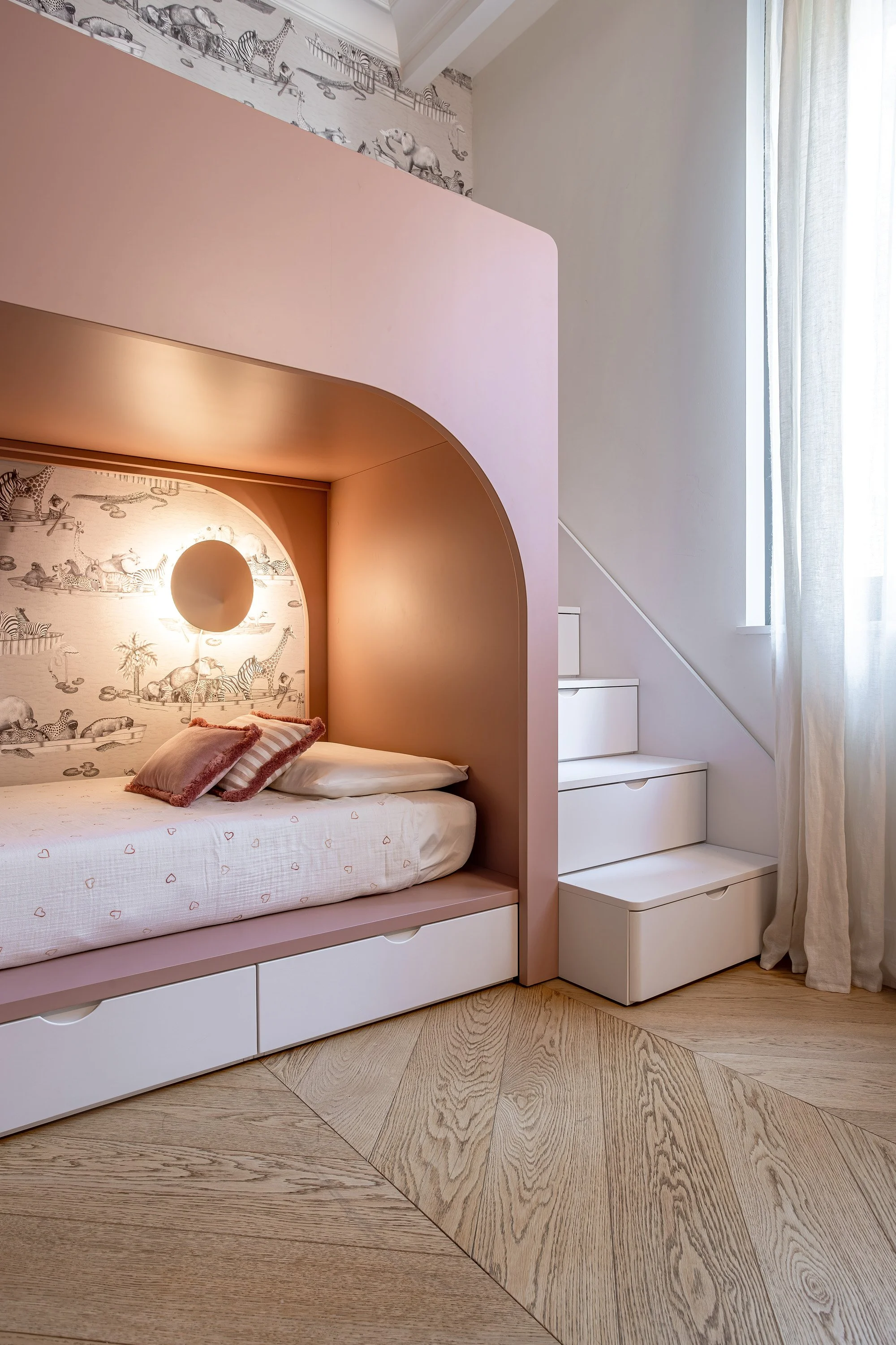 Dettaglio della zona notte con letto in nicchia rosa, contenitori integrati e scala di accesso allo spazio sopraelevato.