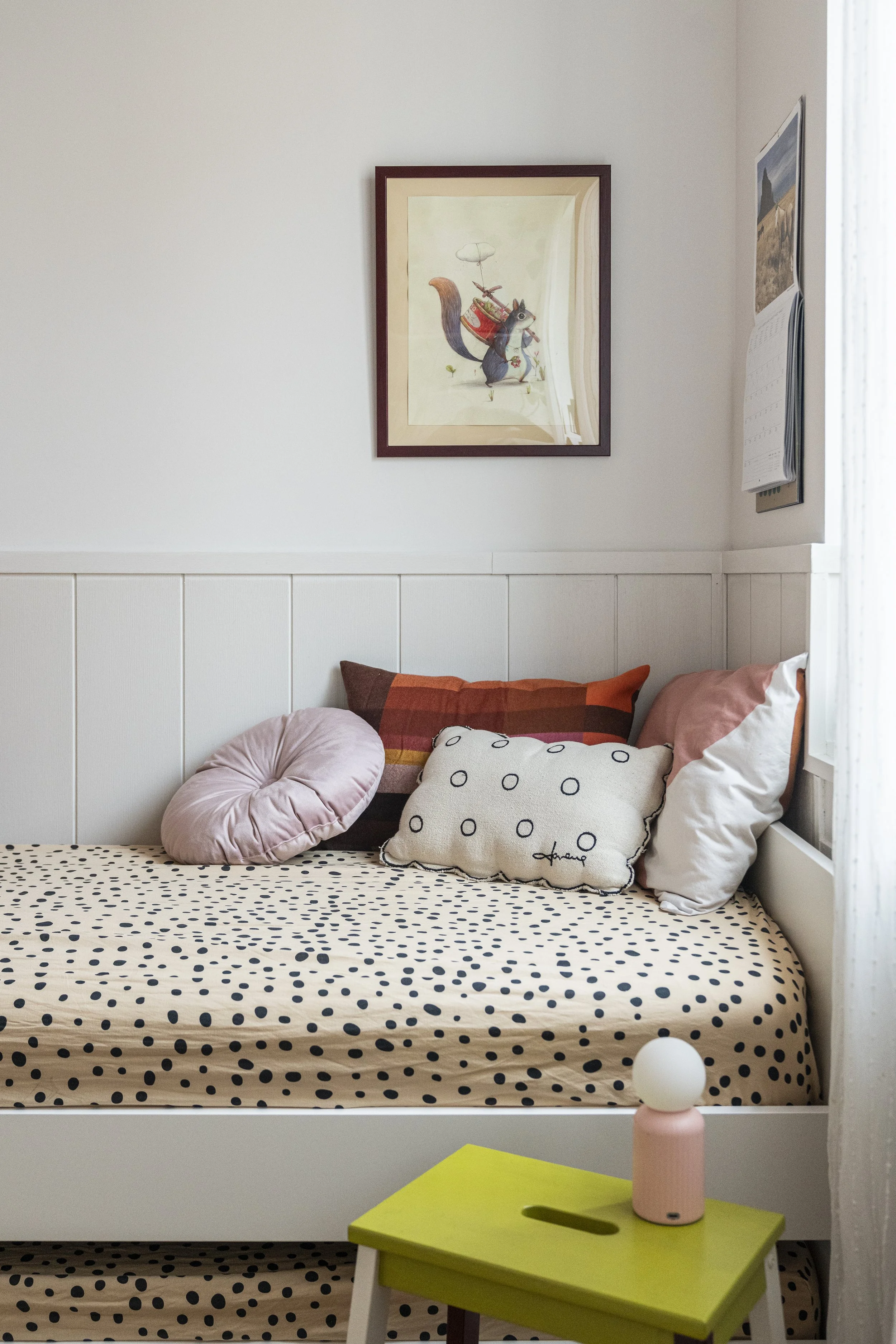 Dettaglio del letto con cuscini decorativi, biancheria a pois e boiserie bianca.