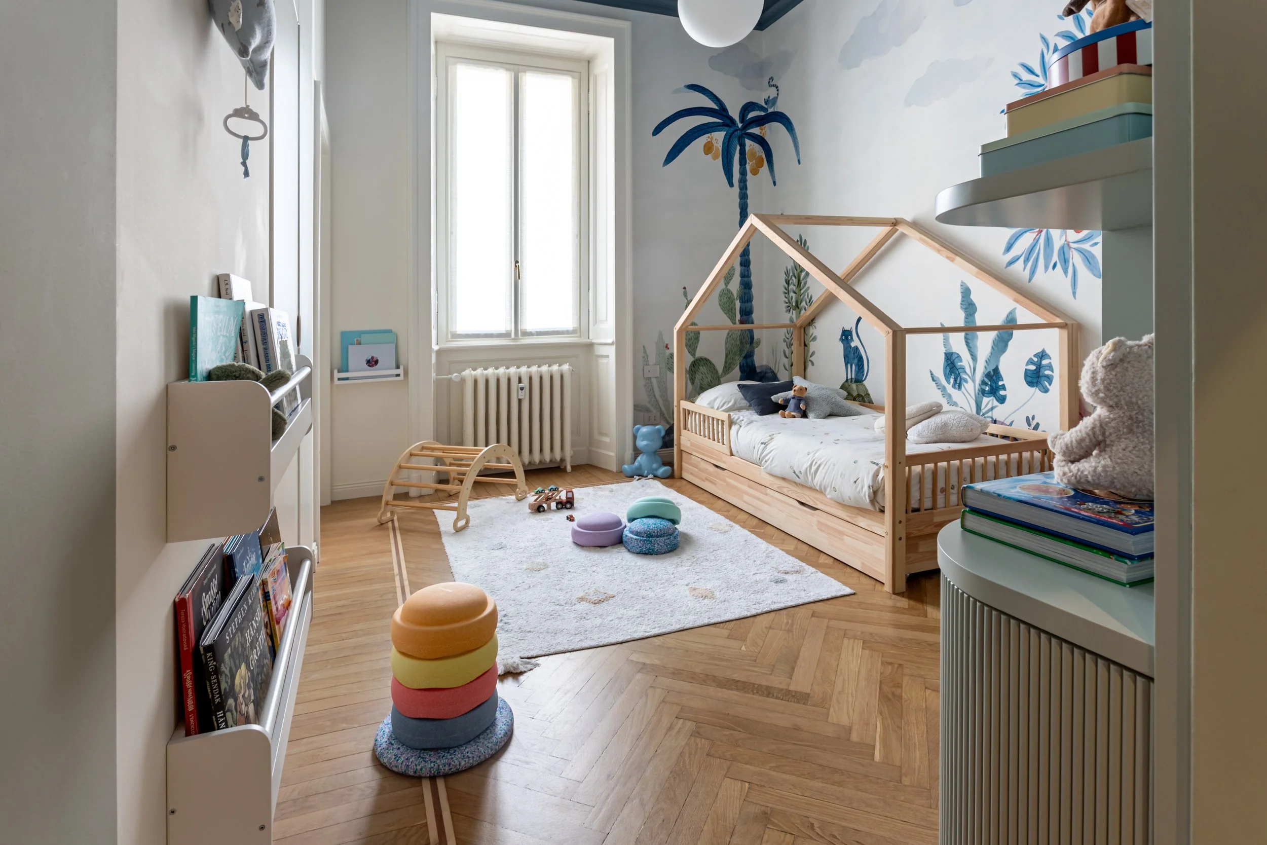 Vista completa della camera con letto a casetta, carta da parati illustrata, zona gioco e parete attrezzata su misura.