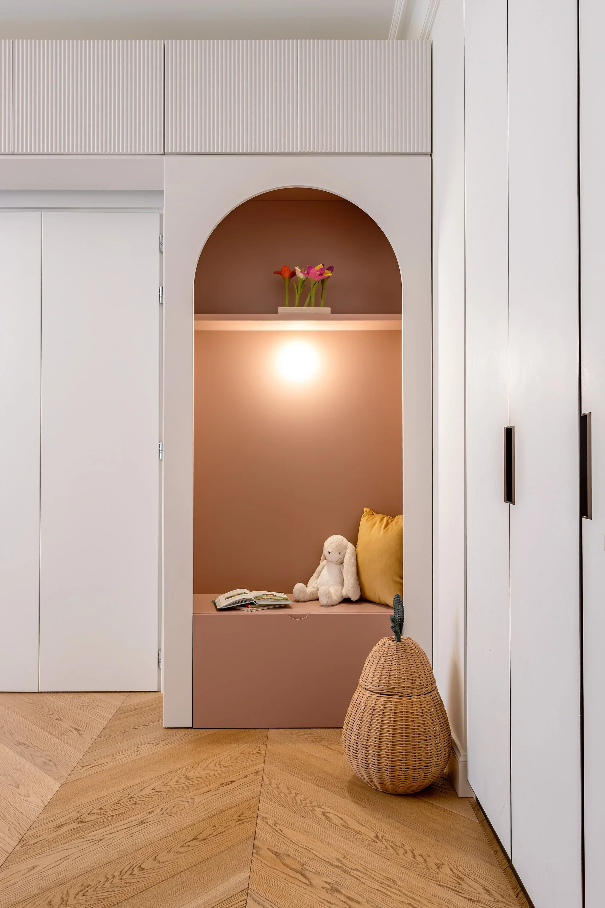Nicchia rosa ad arco integrata nell’armadiatura su misura, utilizzata come angolo lettura e relax.