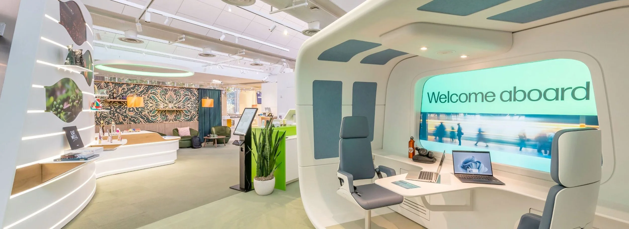 Modern office space with a green wall, wooden furniture, a large screen displaying photo printing instructions, and shelves with decor items.