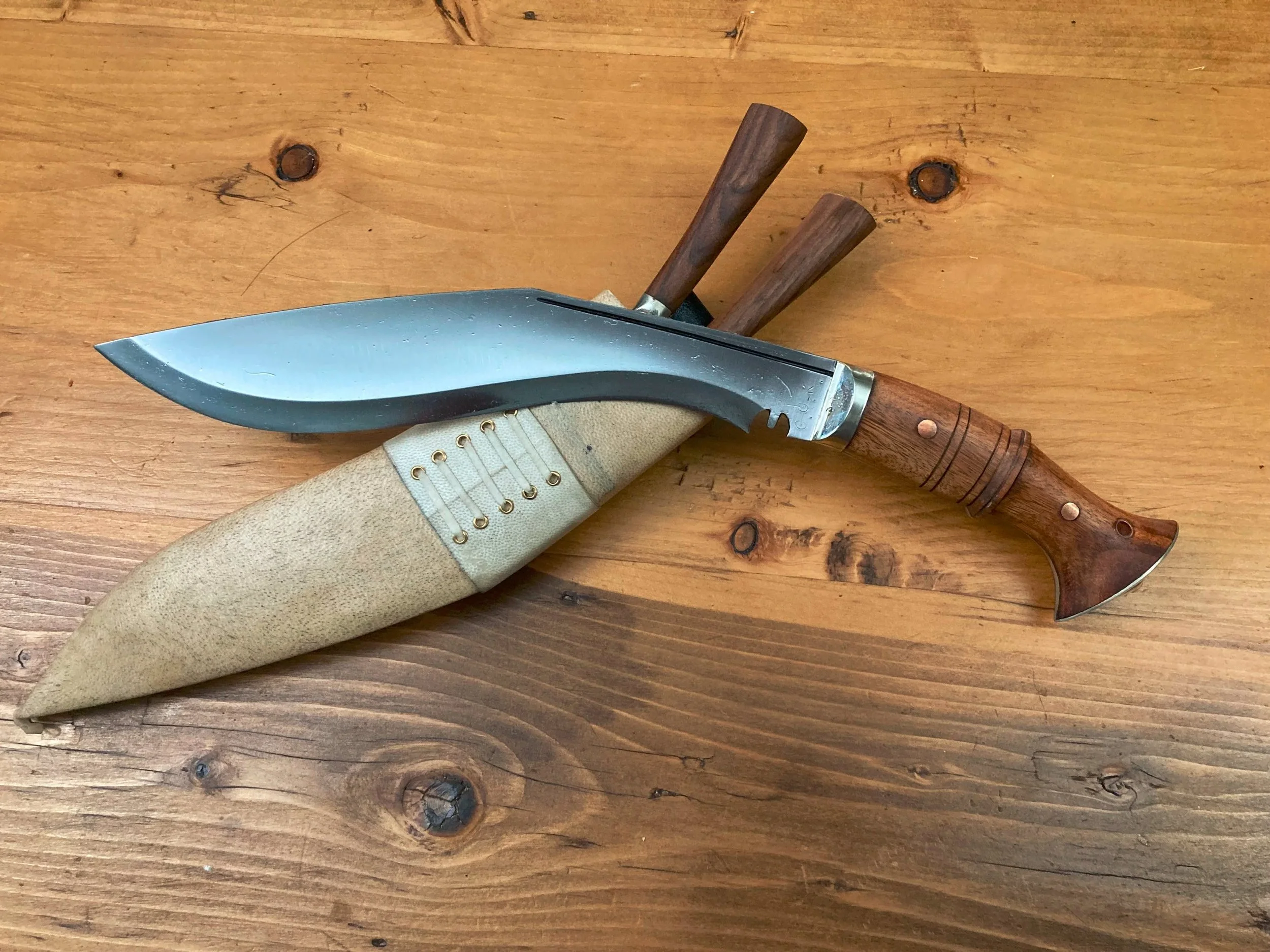 A kukri with a curved blade and black textured handle on a dark surface.