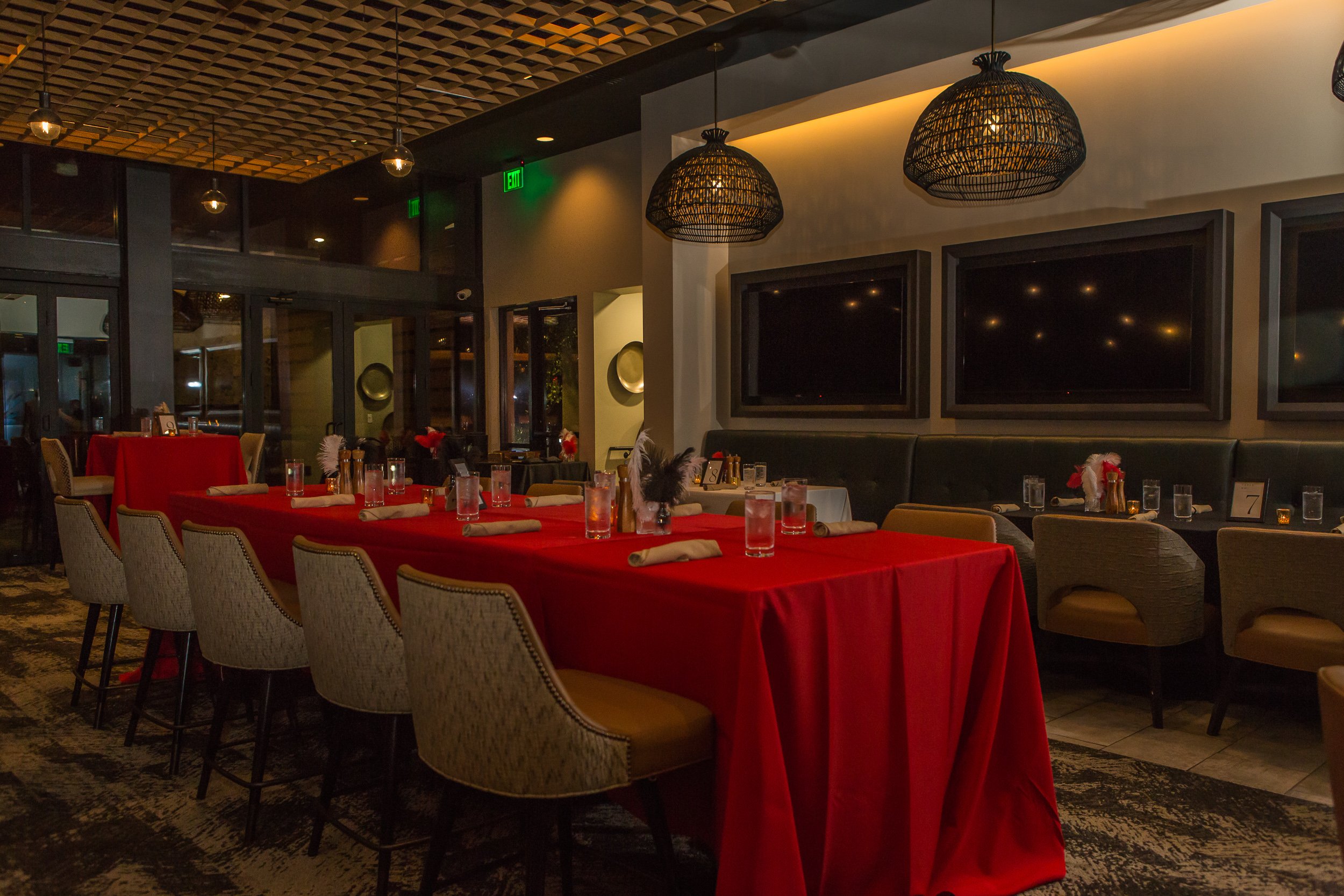 Elegant restaurant dining area at the Gainey Ranch Golf Clubhouse with a long table covered in a red tablecloth, set with glasses, napkins, and centerpieces, surrounded by upholstered chairs, dim lighting, and decorative lighting fixtures.